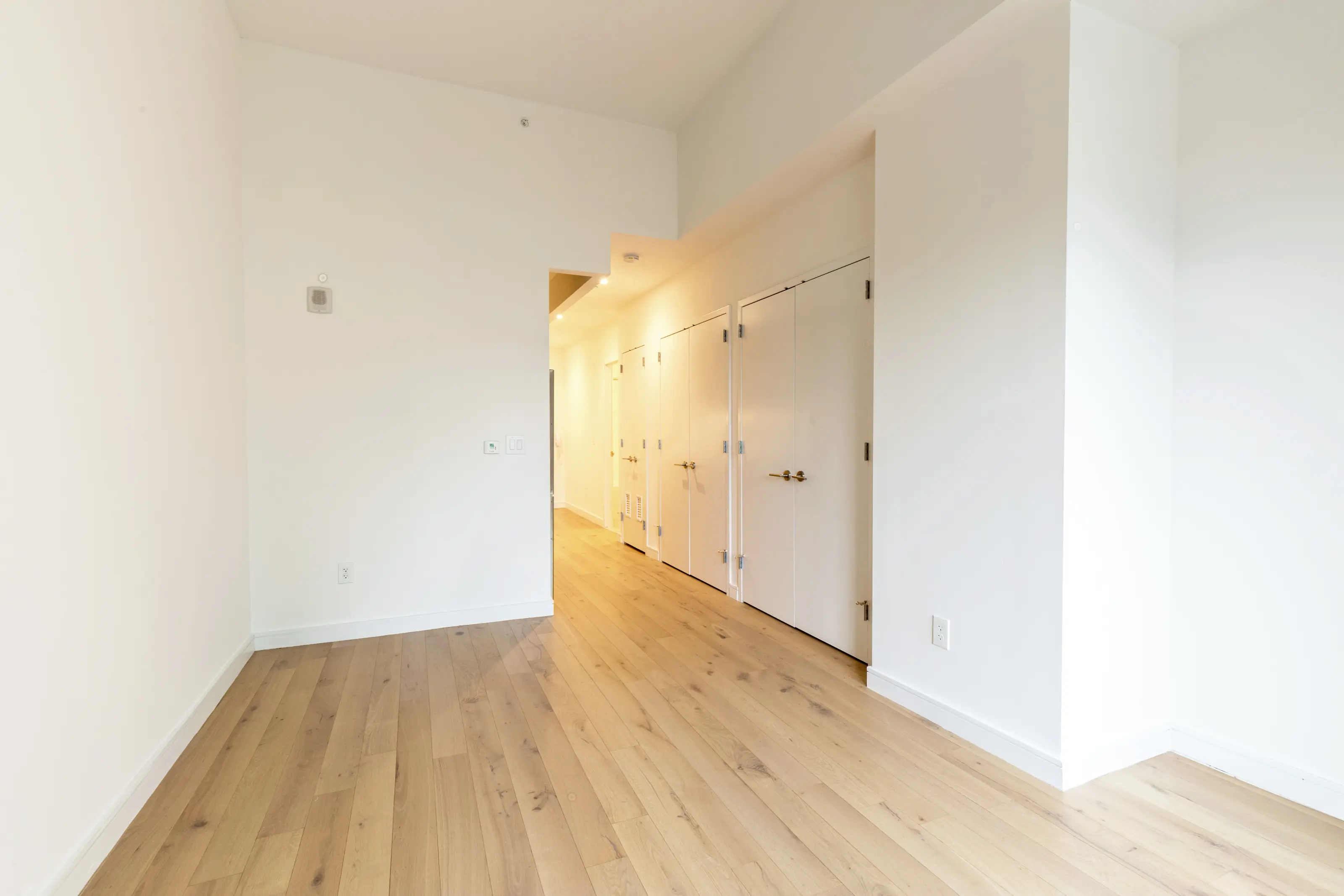 An empty hallway featuring white walls and polished wooden floors, creating a bright and spacious atmosphere.