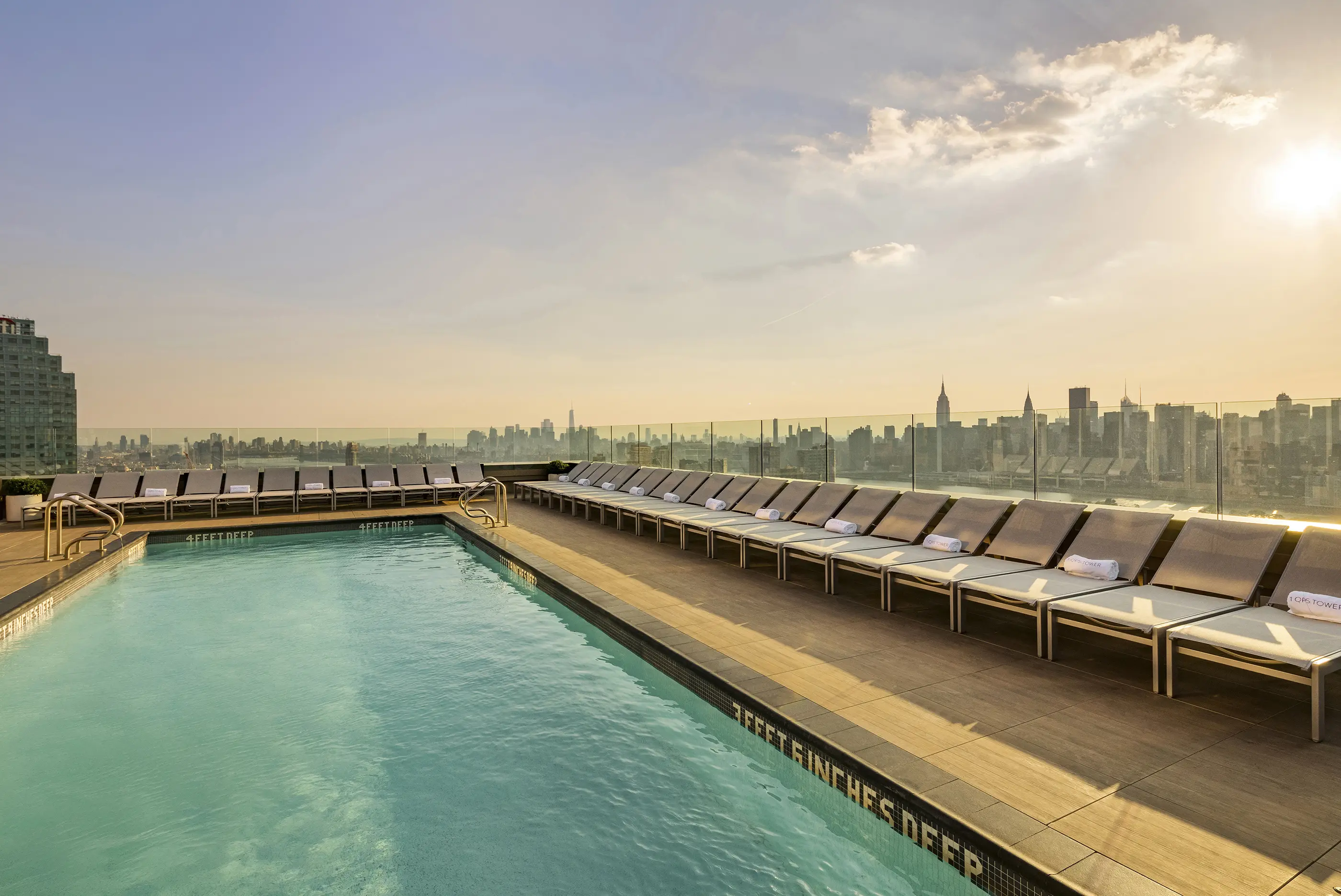 Rooftop pool at the New York hotel, featuring lounge chairs and a city skyline view under a clear blue sky.