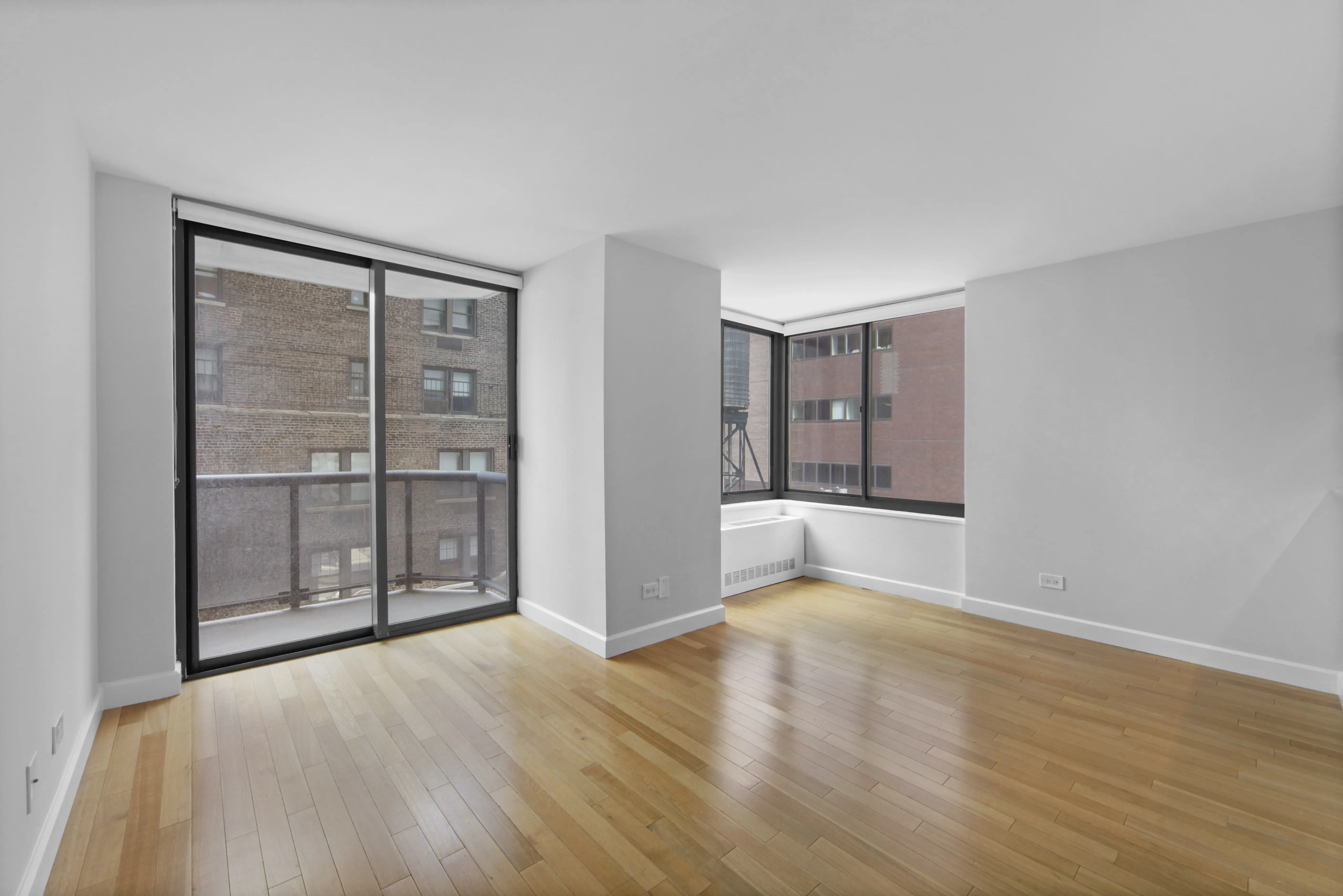 An empty room featuring hardwood floors and large windows allowing natural light to fill the space.