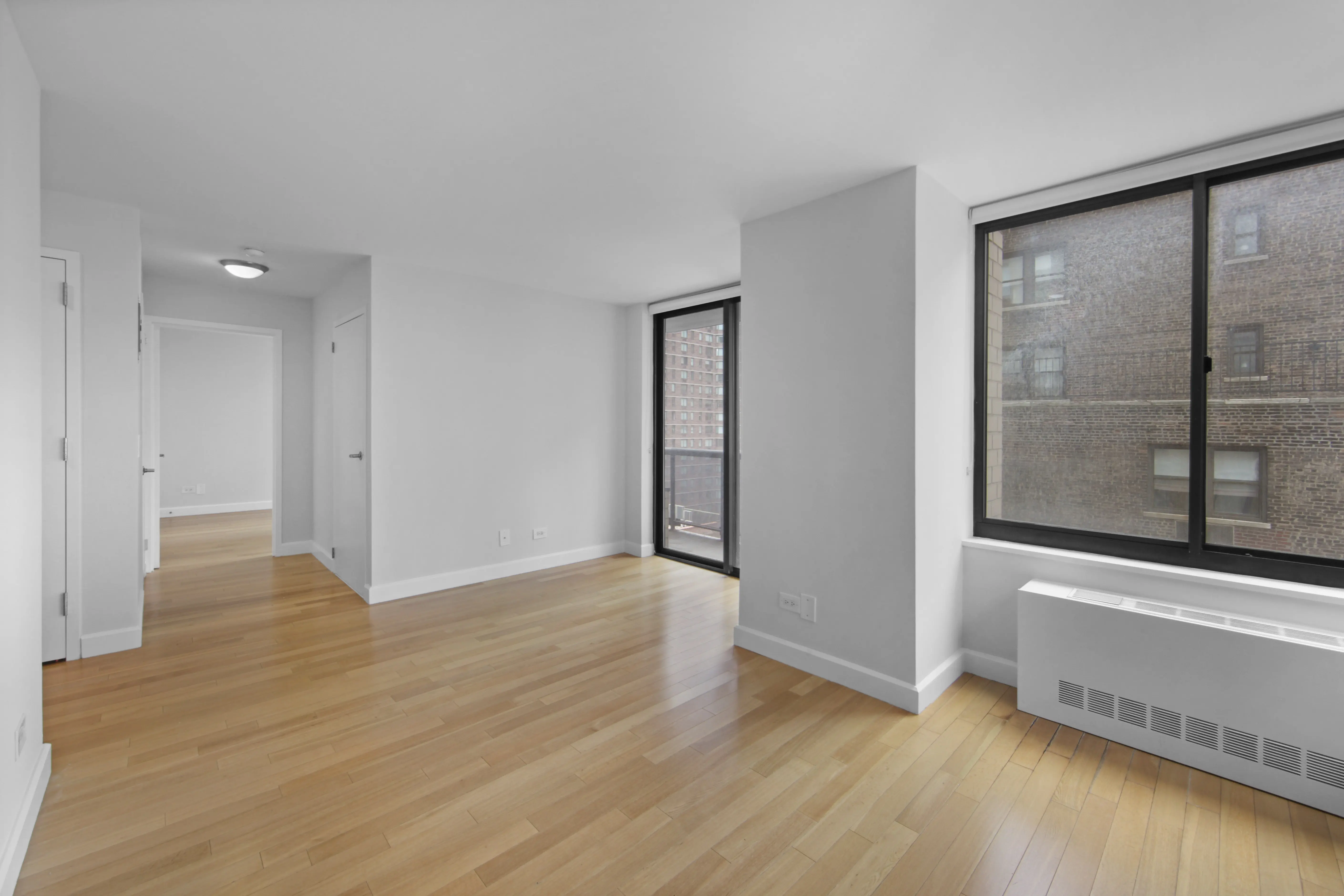 An empty room featuring hardwood floors and large windows allowing natural light to fill the space.