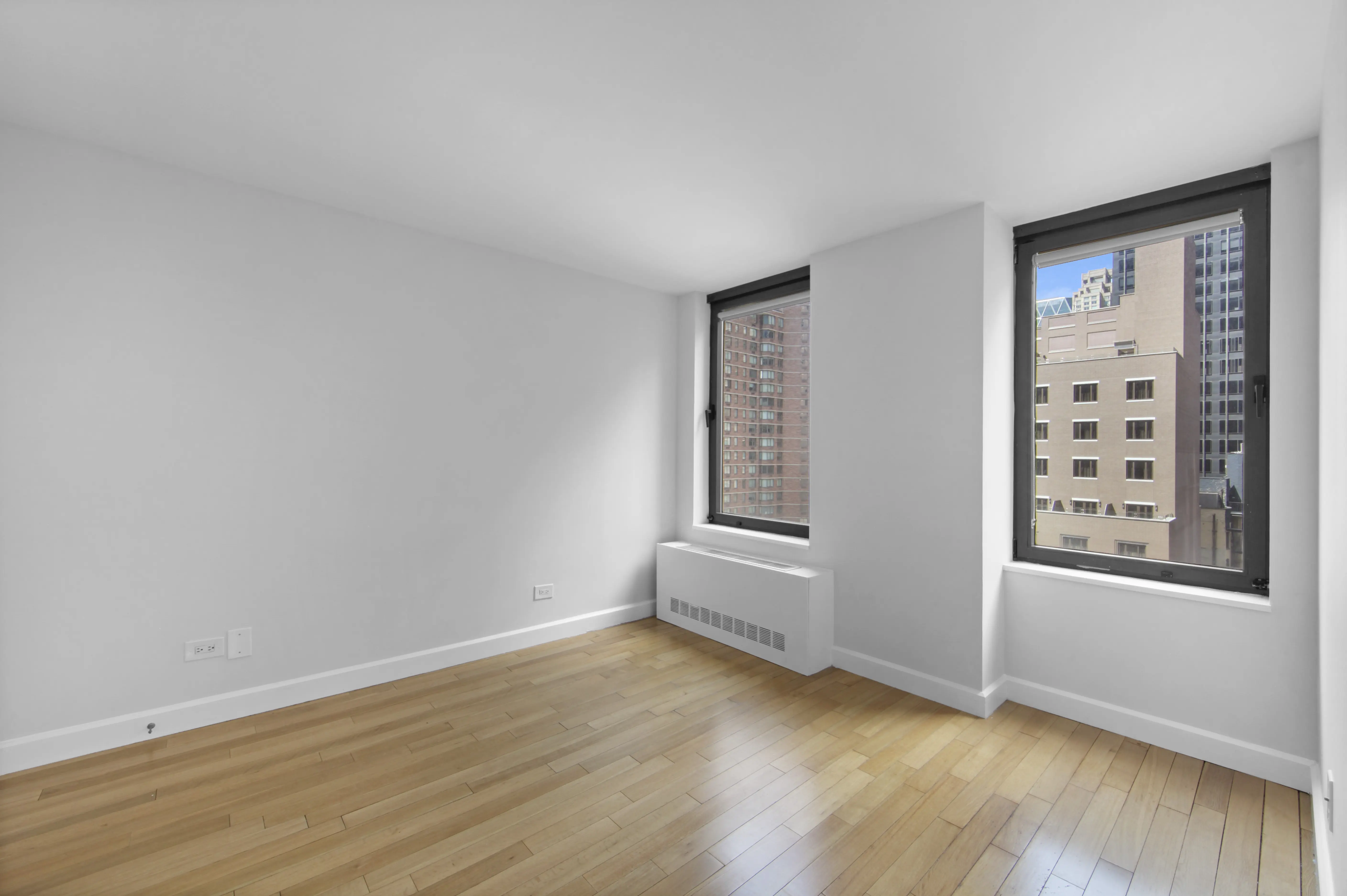 A vacant room with polished hardwood floors and bright windows, creating an open and airy atmosphere.