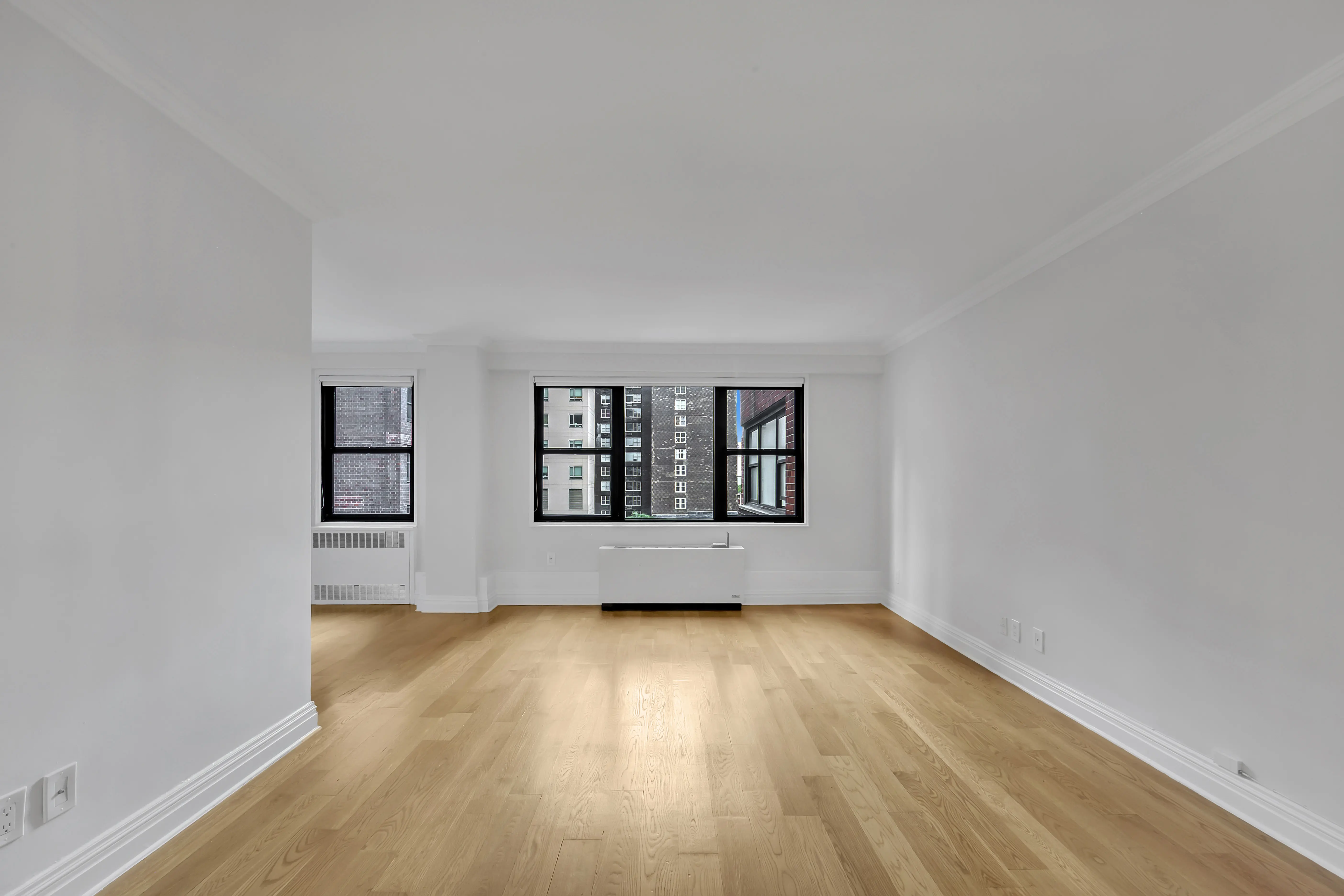 An empty room featuring hardwood floors and large windows allowing natural light to enter.