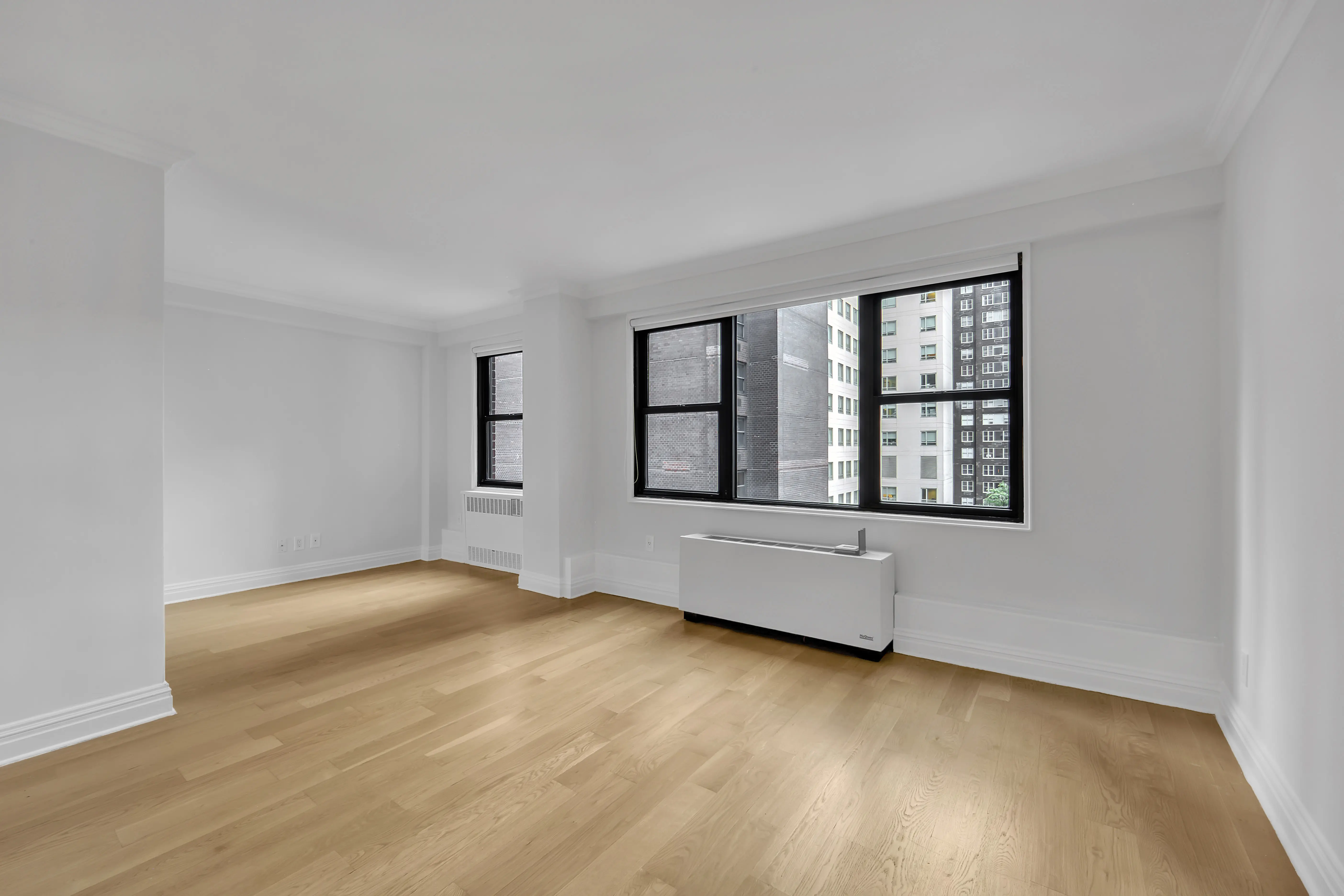 An empty room featuring hardwood floors and large windows allowing natural light to enter.