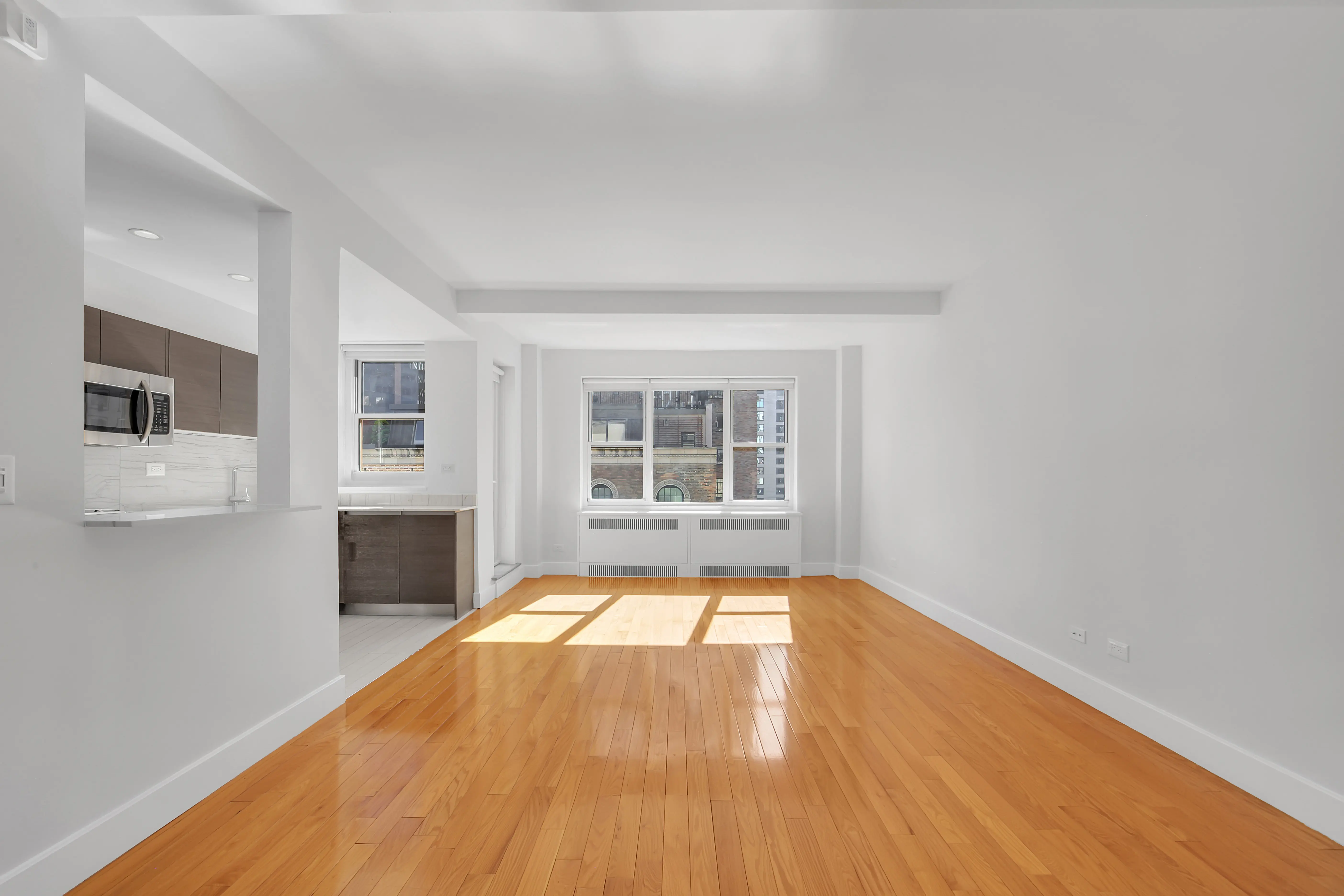 An empty apartment featuring hardwood floors and white walls, creating a bright and spacious atmosphere.