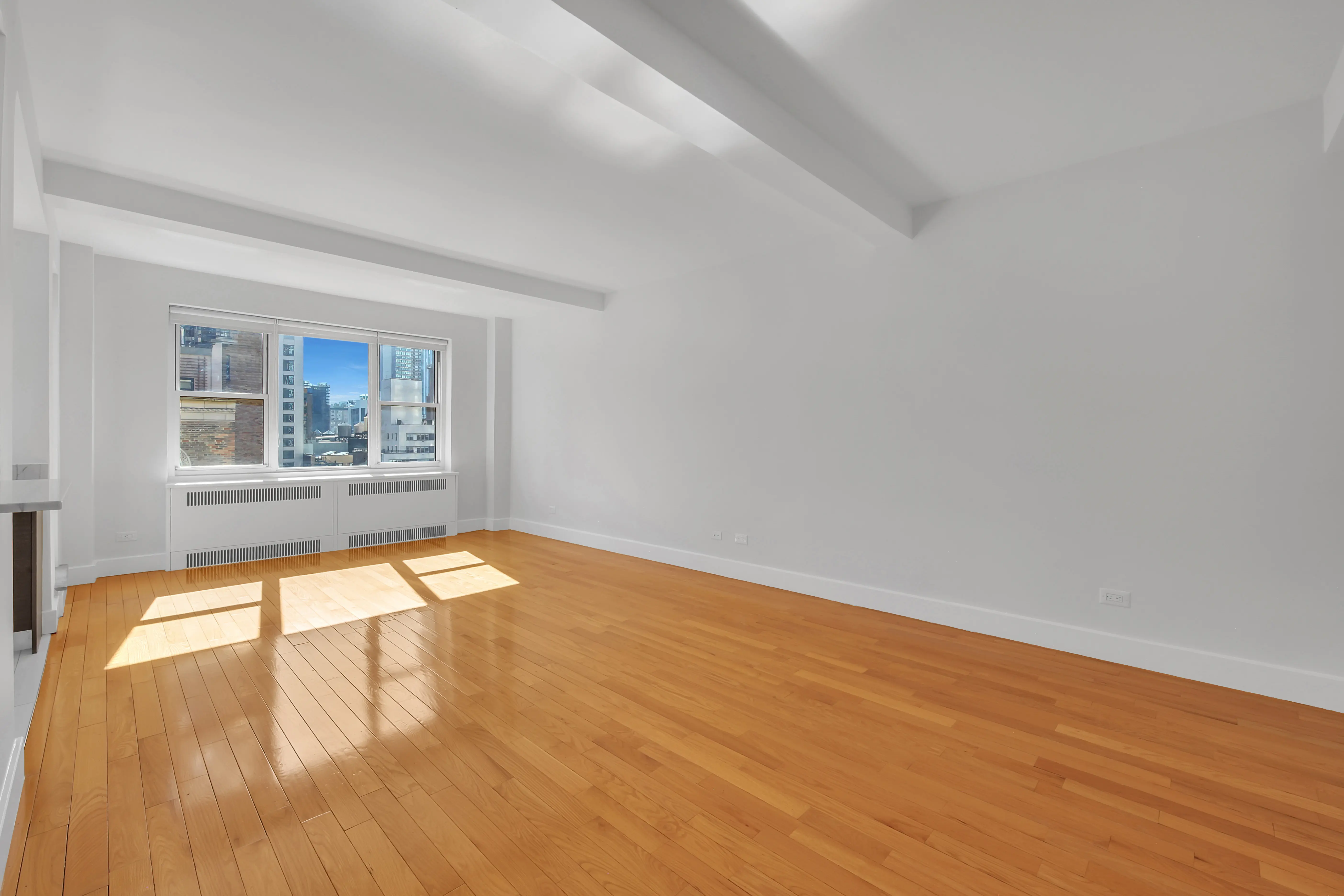An empty room featuring hardwood floors and large windows allowing natural light to enter.