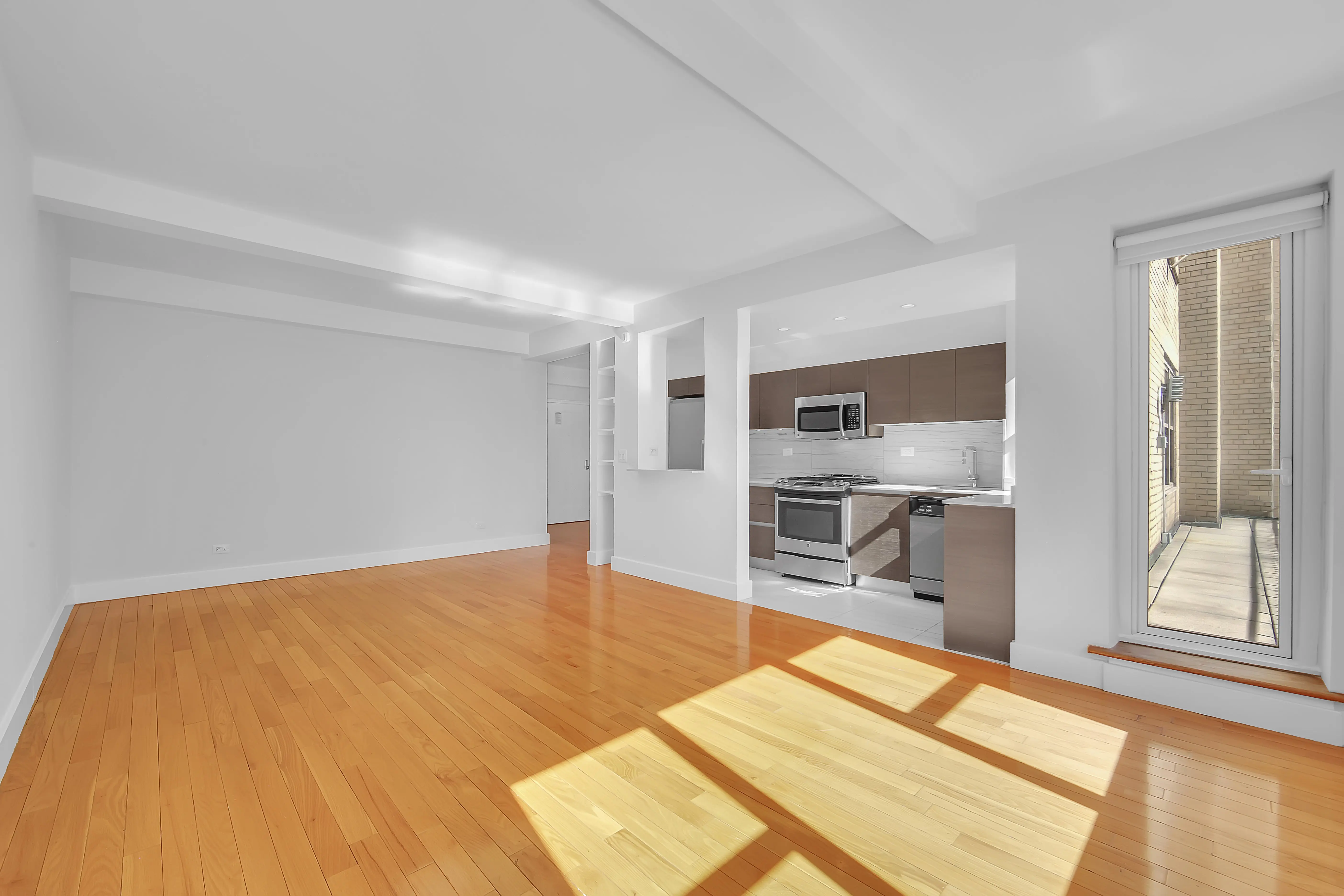 An empty apartment featuring hardwood floors and a modern kitchen, showcasing a spacious and minimalist design.