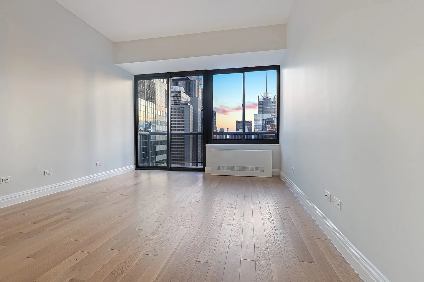 An empty room with hardwood floors, featuring large windows that offer a view of the city skyline.