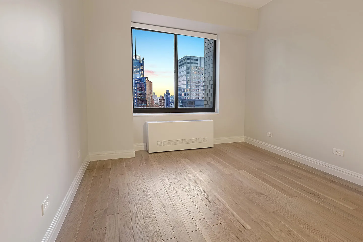 An empty room featuring hardwood floors and a large window allowing natural light to enter.