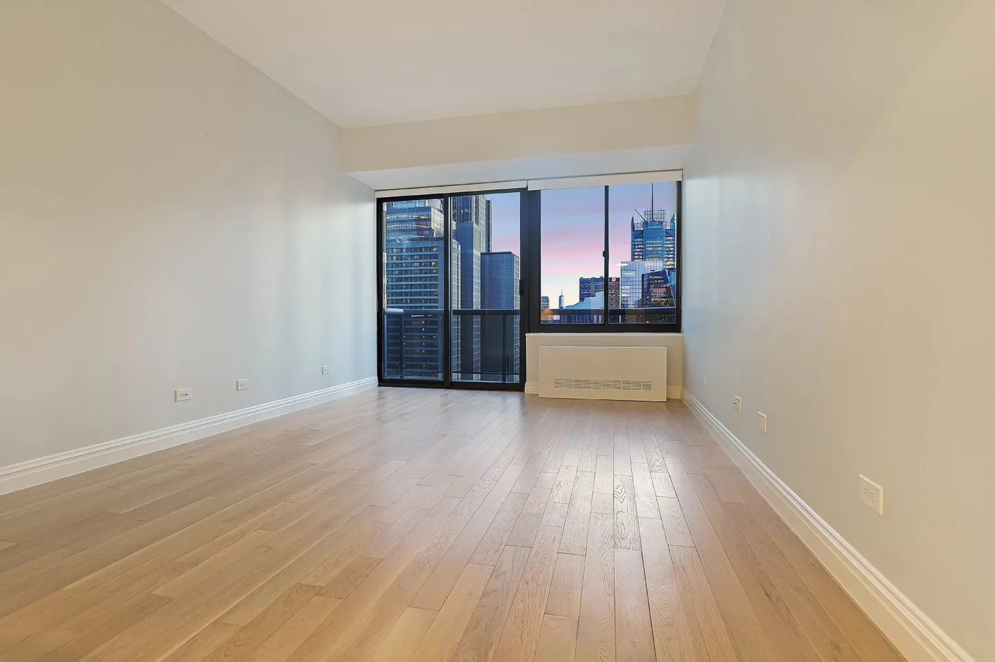 A vacant room with polished hardwood floors and a spacious window, creating an airy atmosphere.