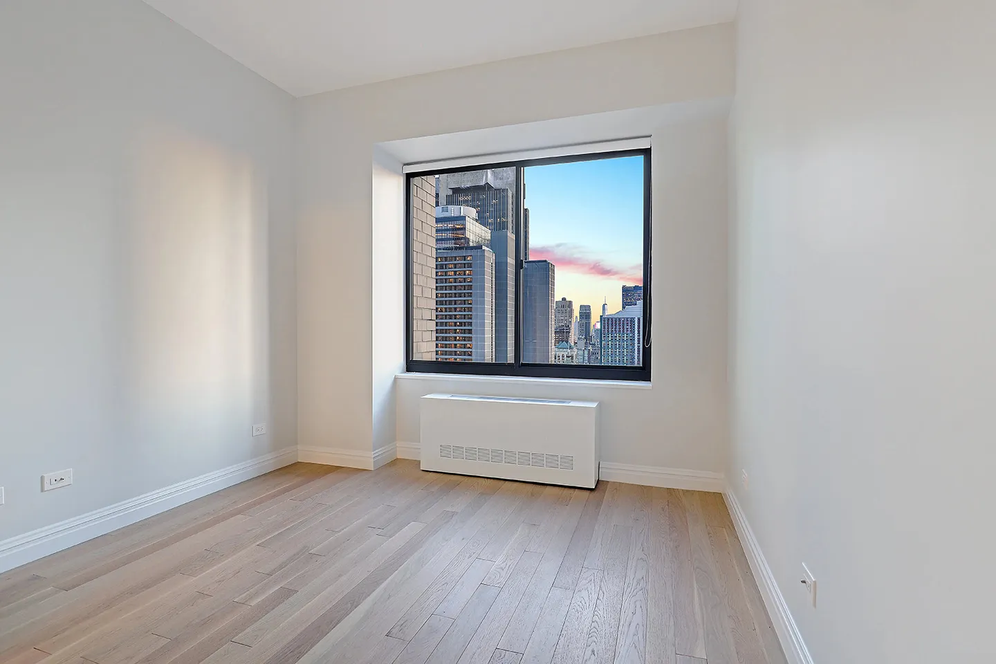 A vacant room with polished hardwood floors and a window, creating a bright and open atmosphere.