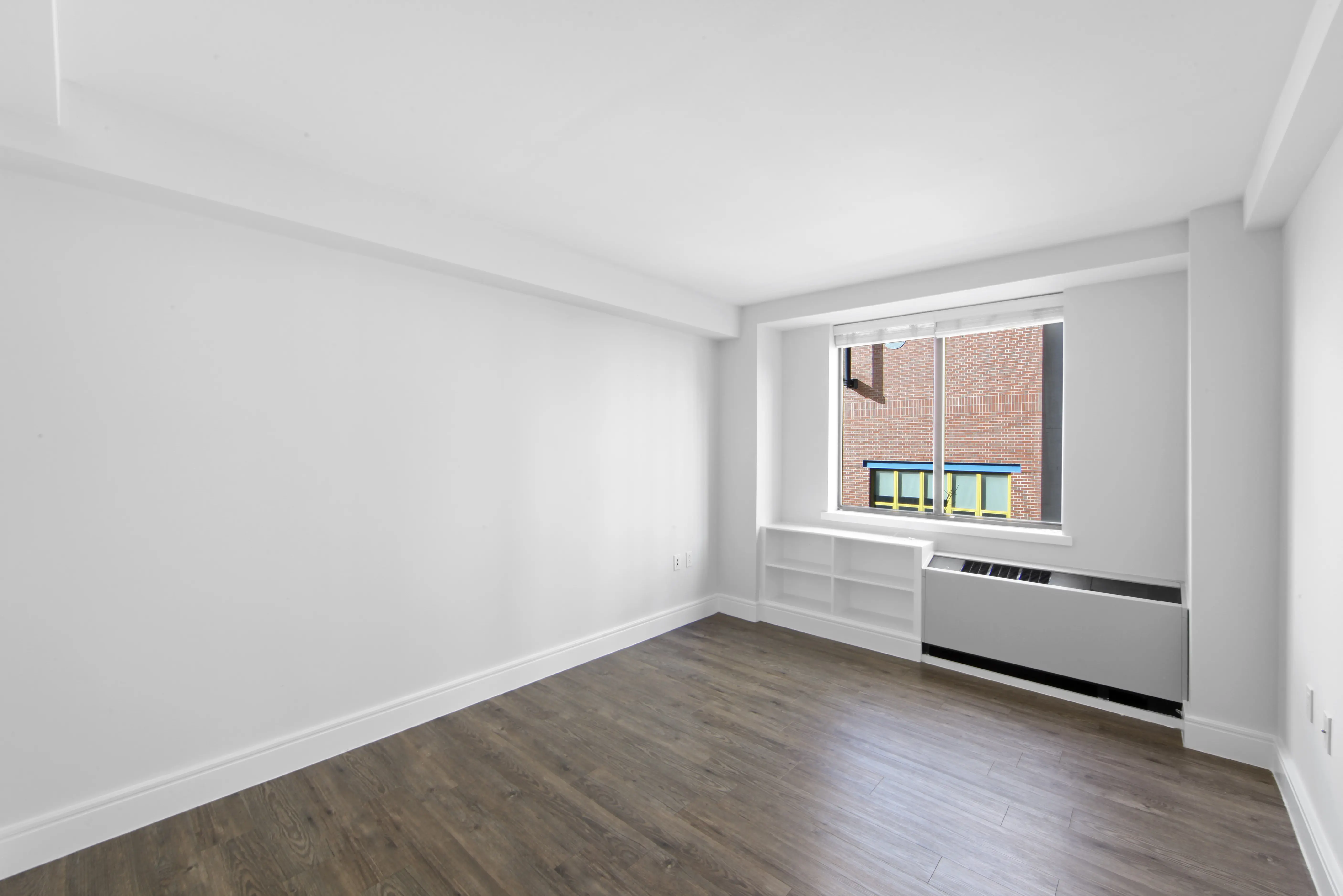 An empty room featuring hardwood floors and a large window allowing natural light to enter.