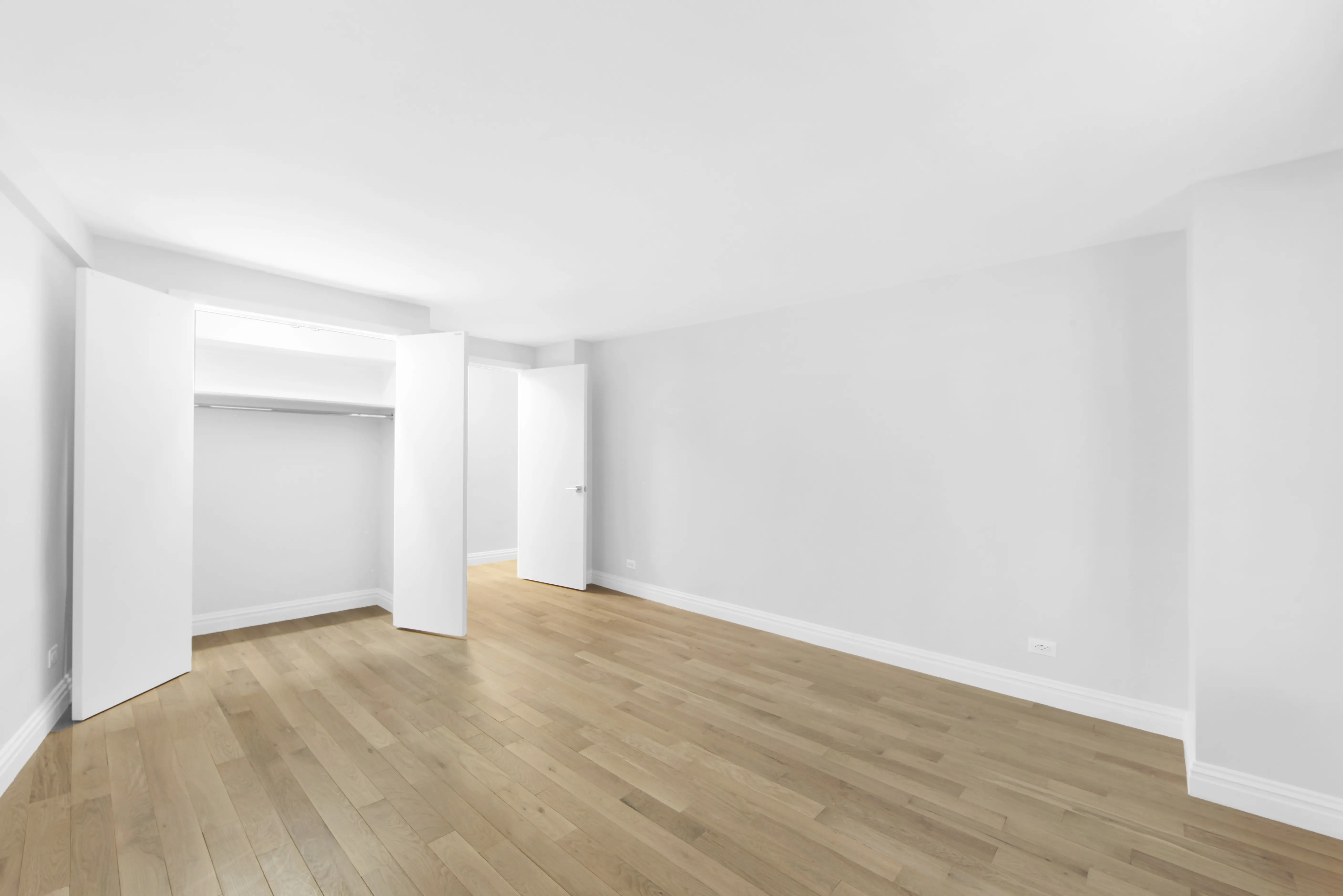 An empty room featuring white walls and polished wooden floors, creating a bright and spacious atmosphere.