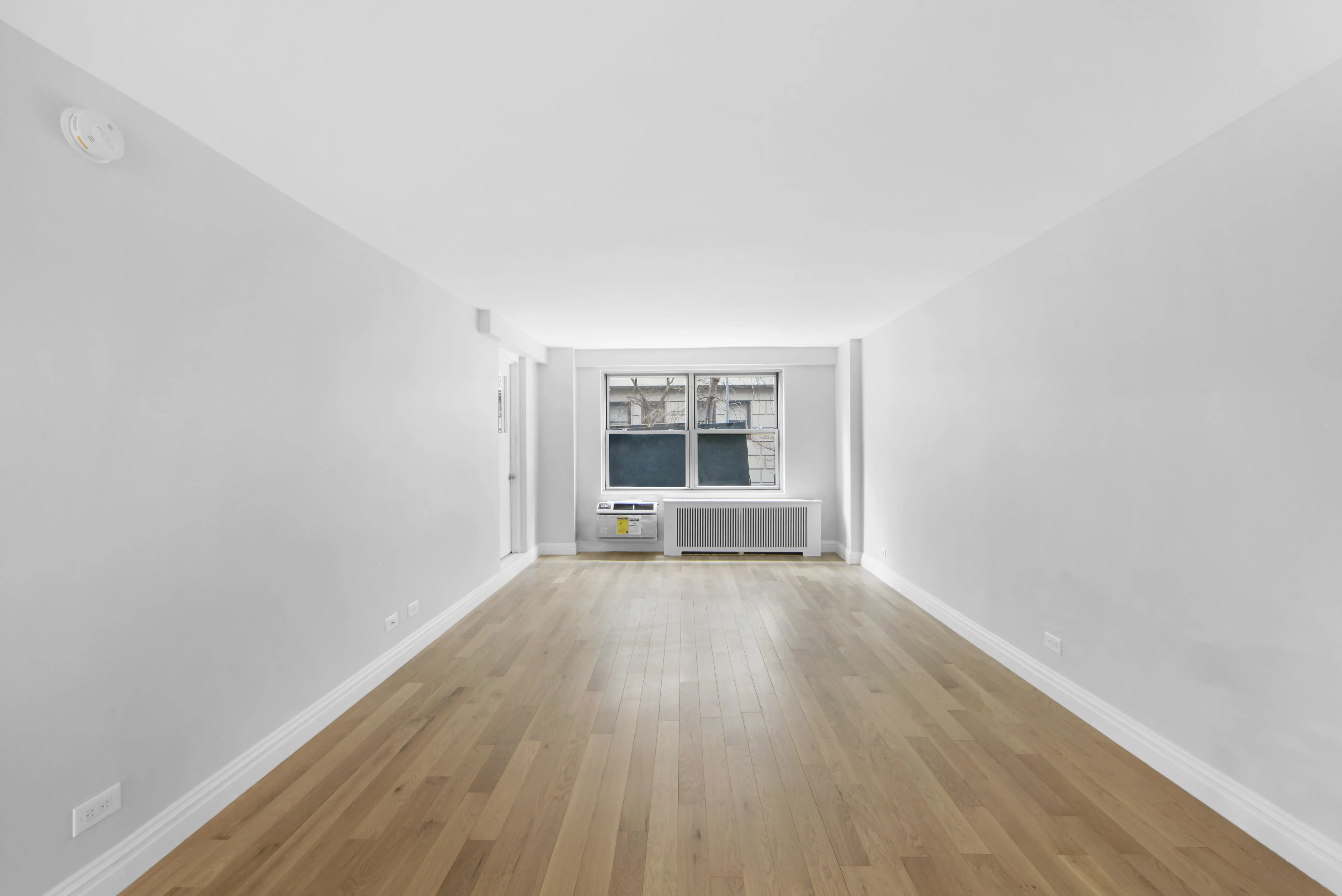 An empty hallway featuring white walls and polished wooden floors, creating a bright and spacious atmosphere.