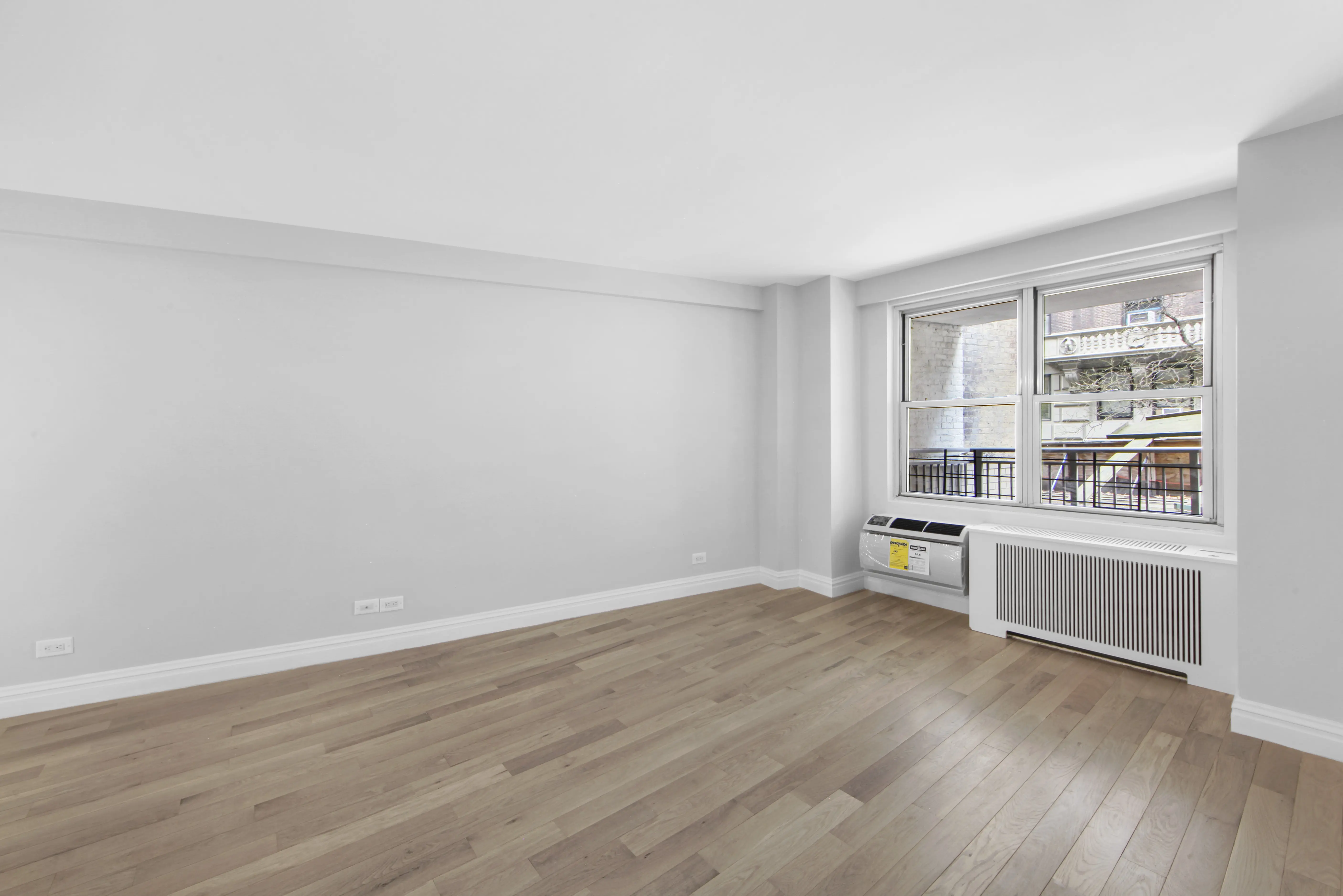 An empty room featuring hardwood floors and a large window allowing natural light to enter.