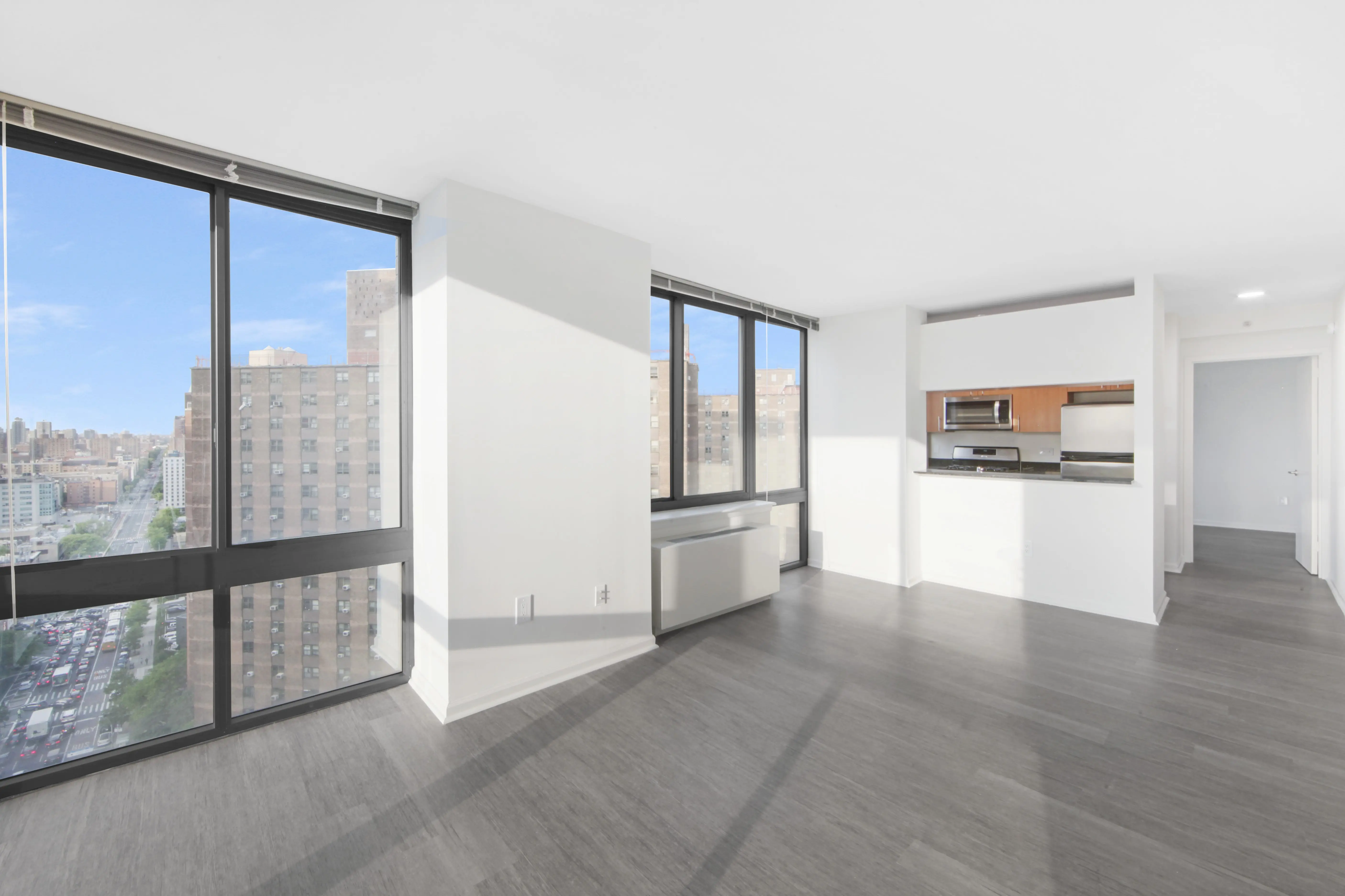 An empty apartment featuring large windows and polished hardwood floors, creating a bright and spacious atmosphere.