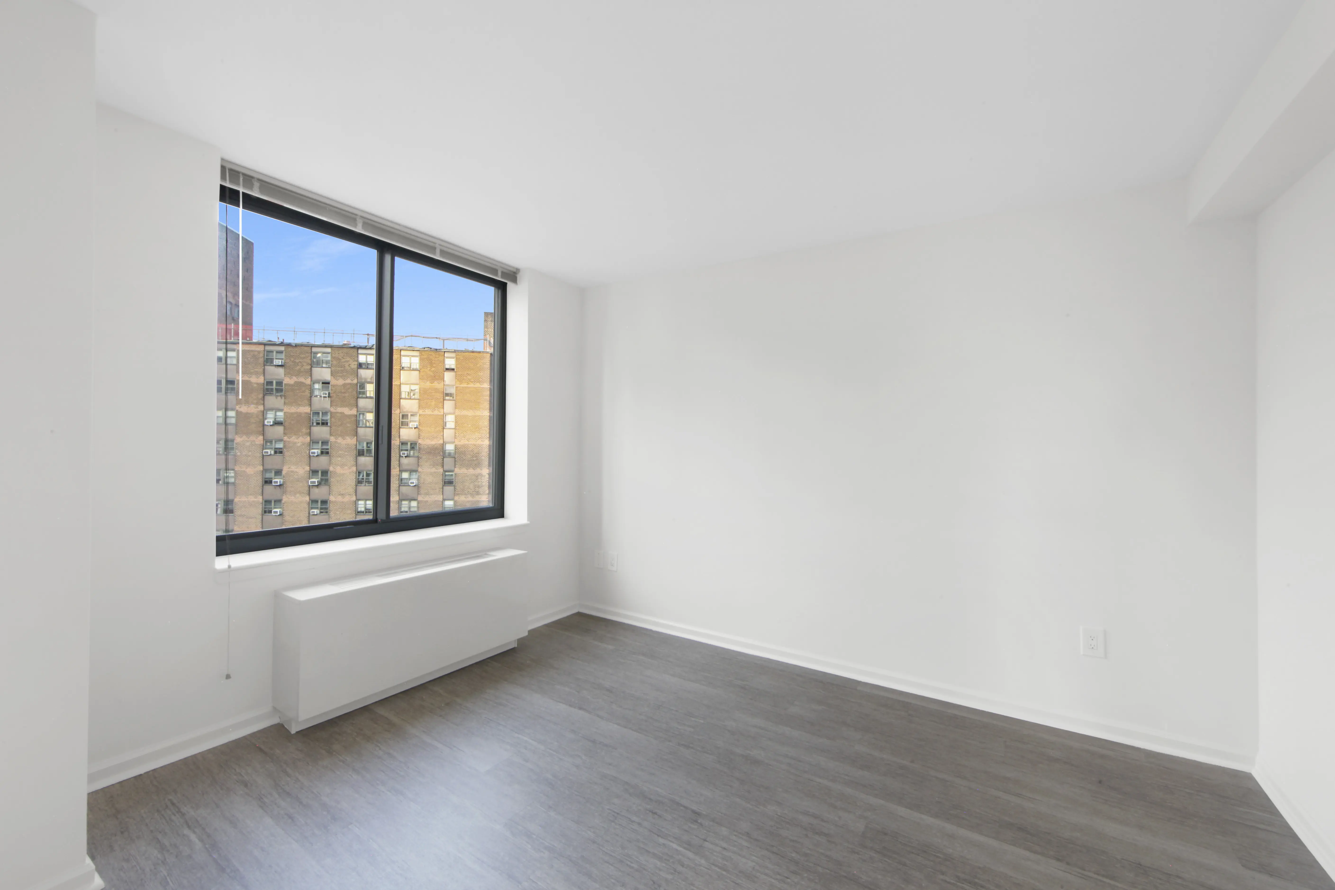 An empty room featuring hardwood floors and a large window allowing natural light to enter.