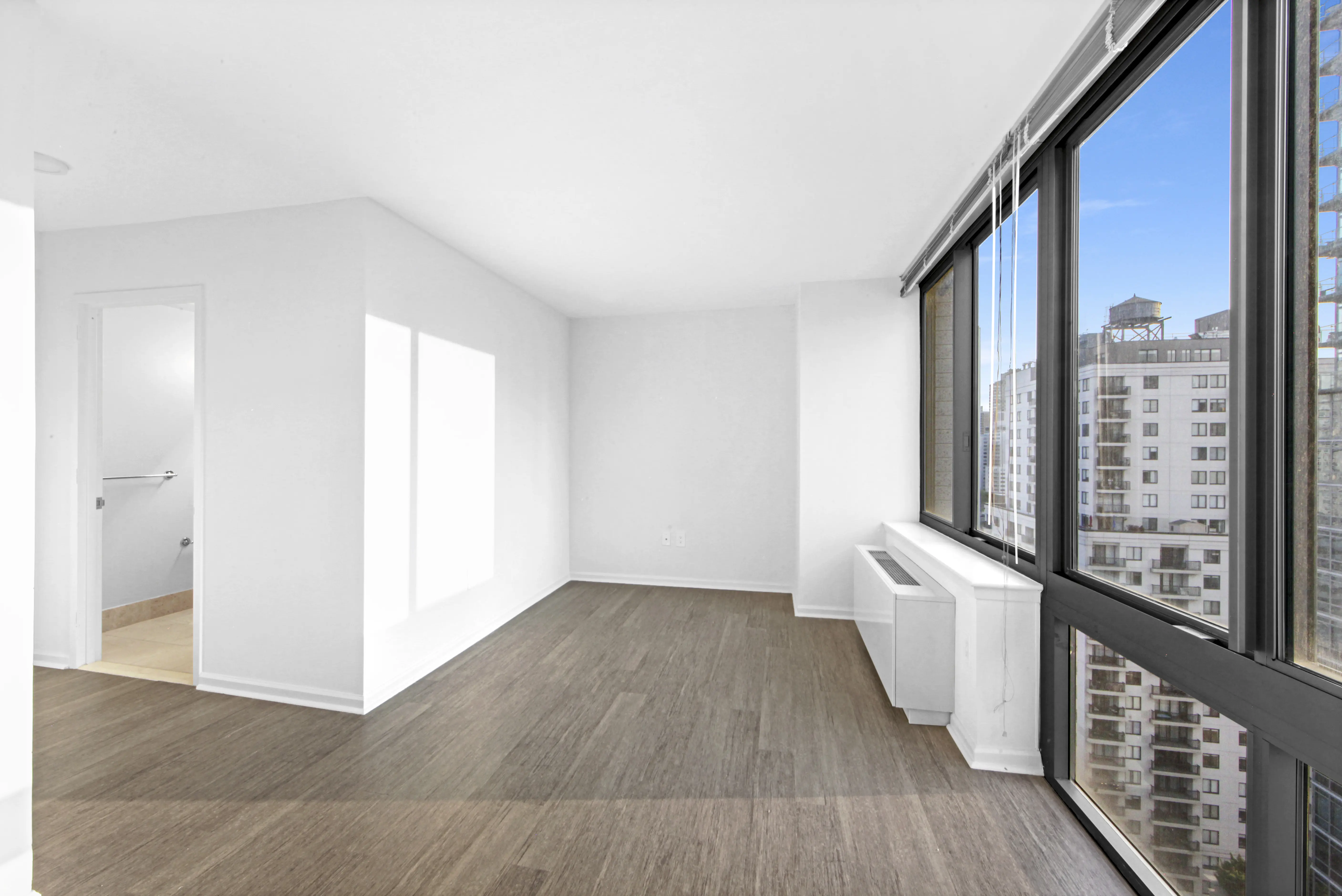 An expansive, vacant room with polished hardwood floors and large windows that brighten the area with sunlight.