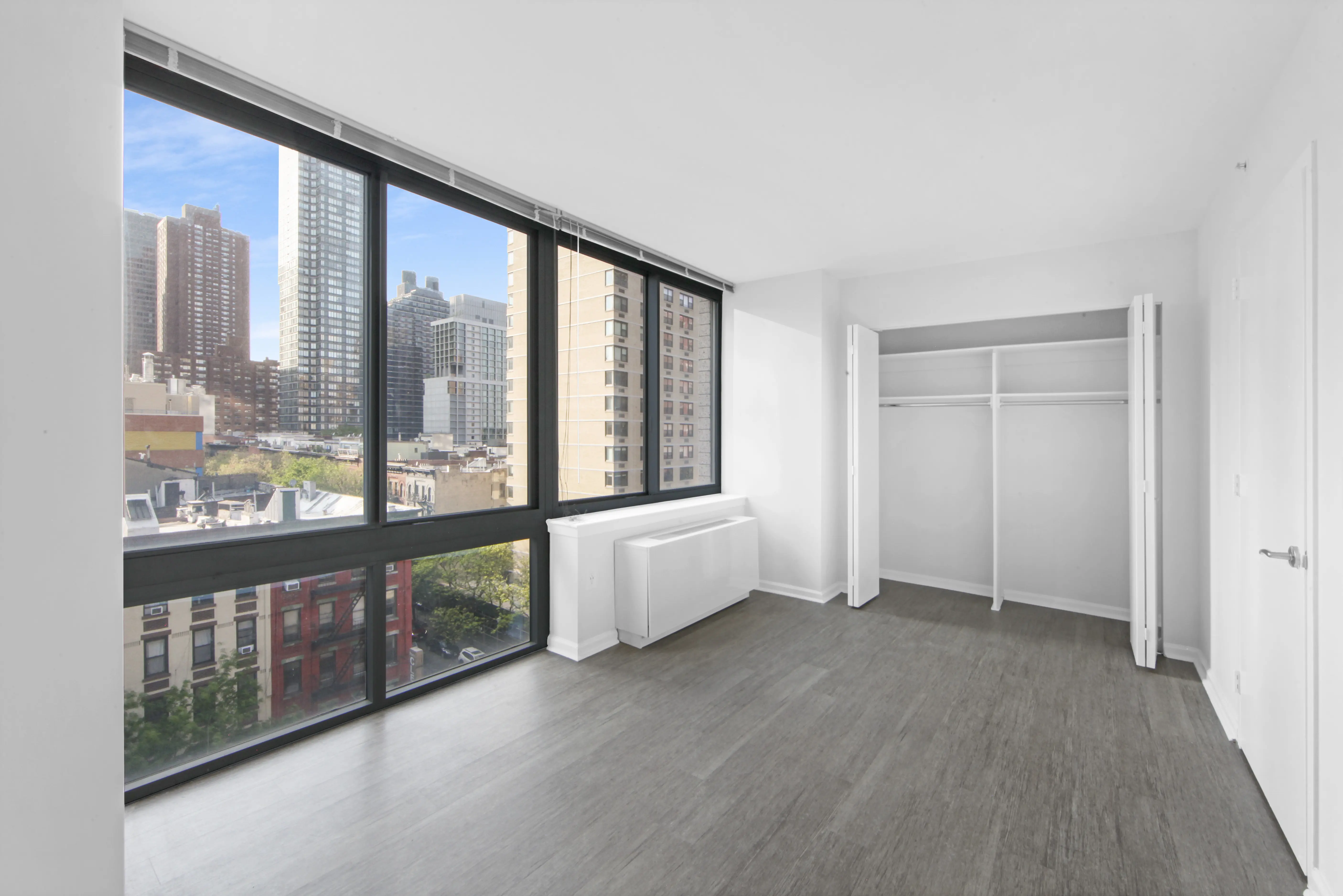 An expansive, vacant room with floor-to-ceiling windows showcasing a vibrant cityscape outside.