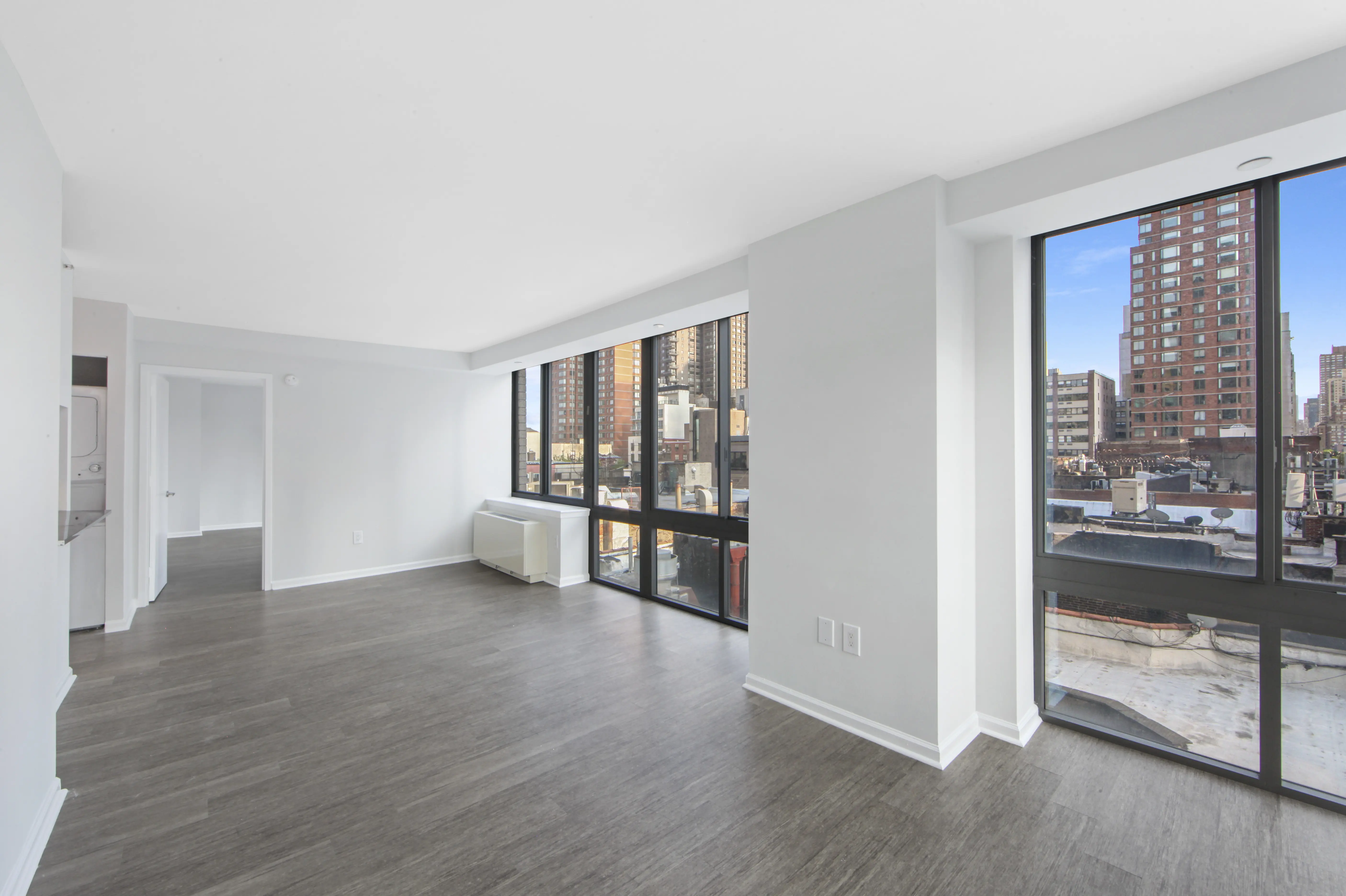 An empty apartment featuring hardwood floors and large windows, allowing ample natural light to fill the space.