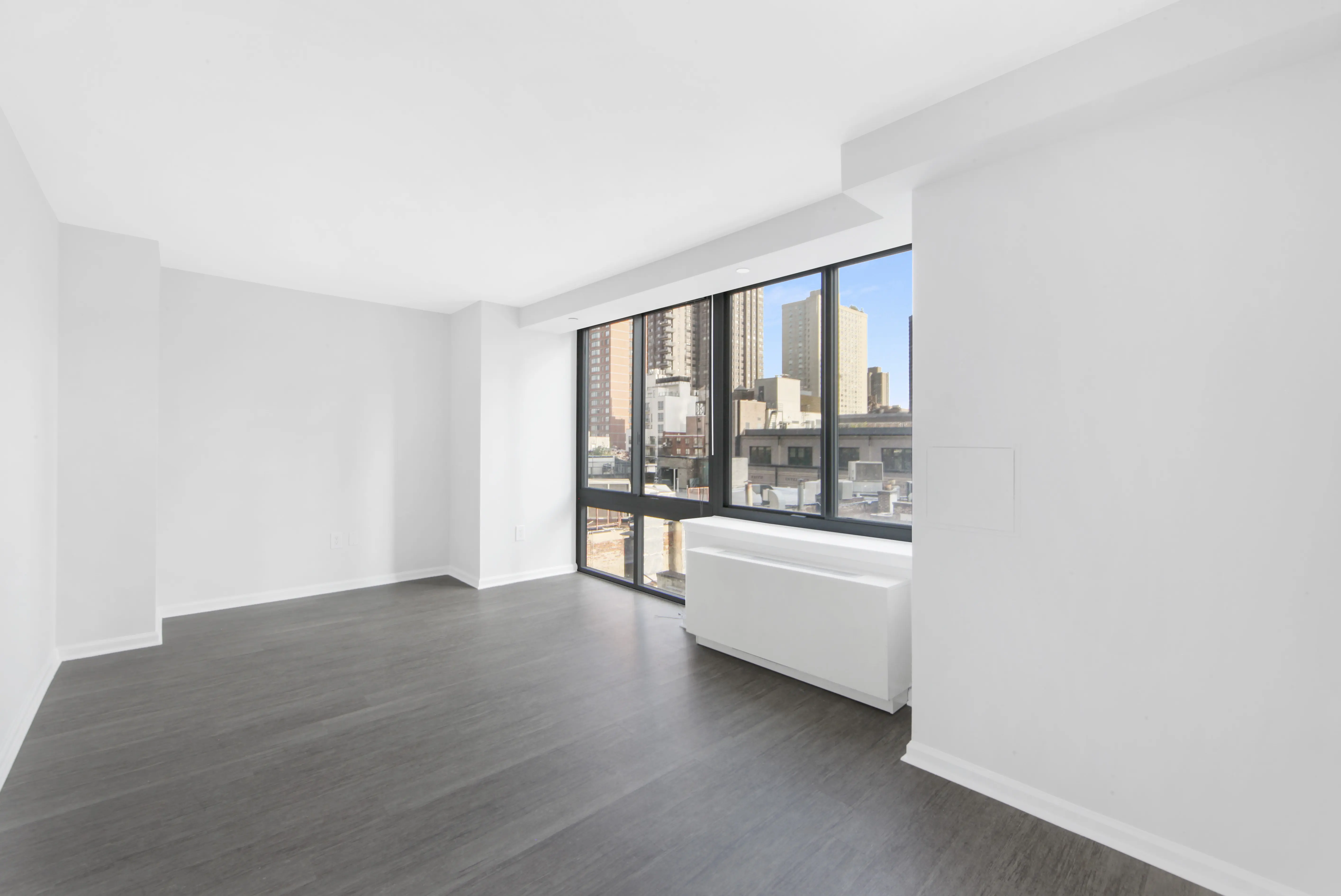 A vacant room with polished hardwood floors and expansive windows, creating a bright and airy atmosphere.