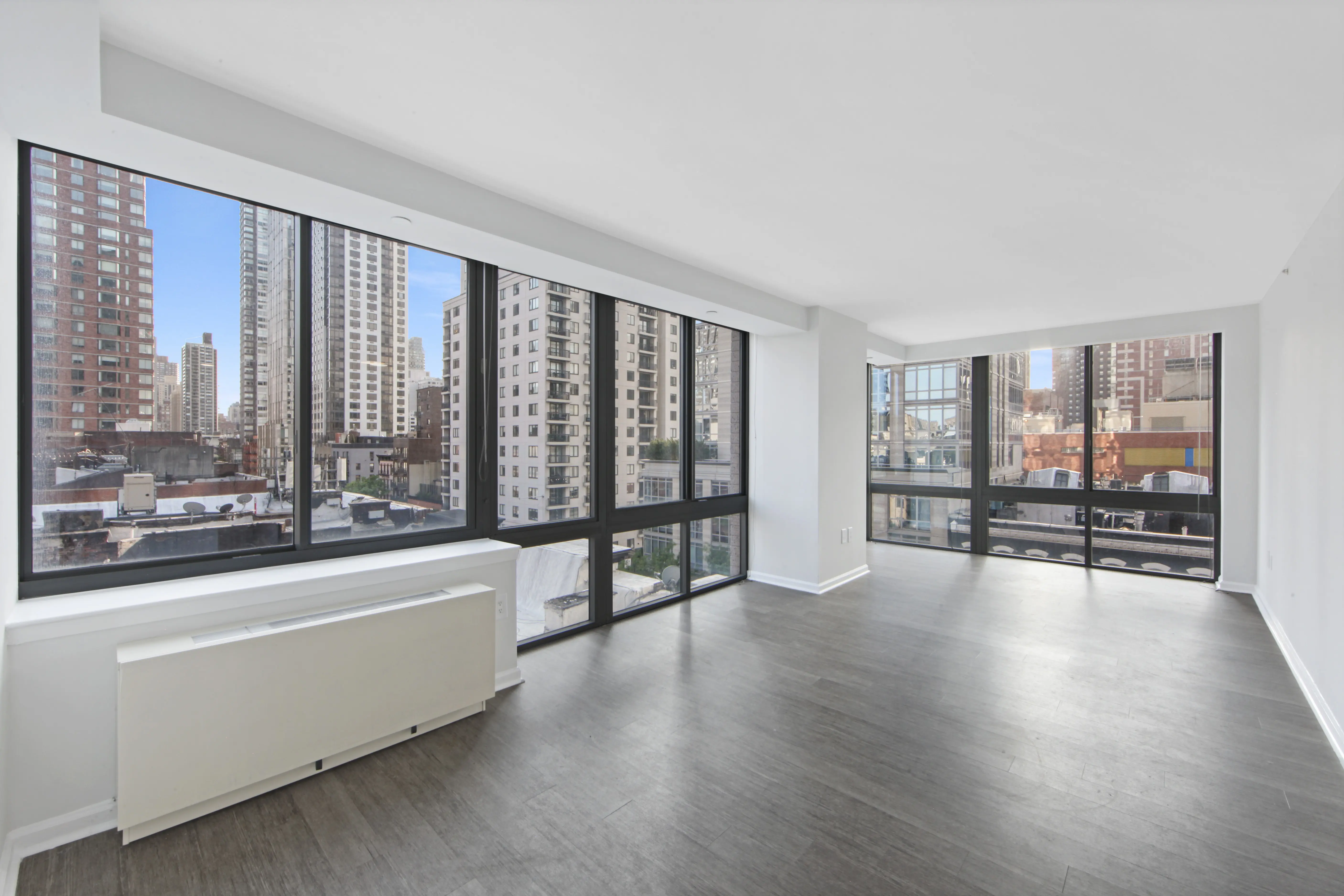 An empty apartment featuring large windows and polished hardwood floors, showcasing a bright and spacious interior.