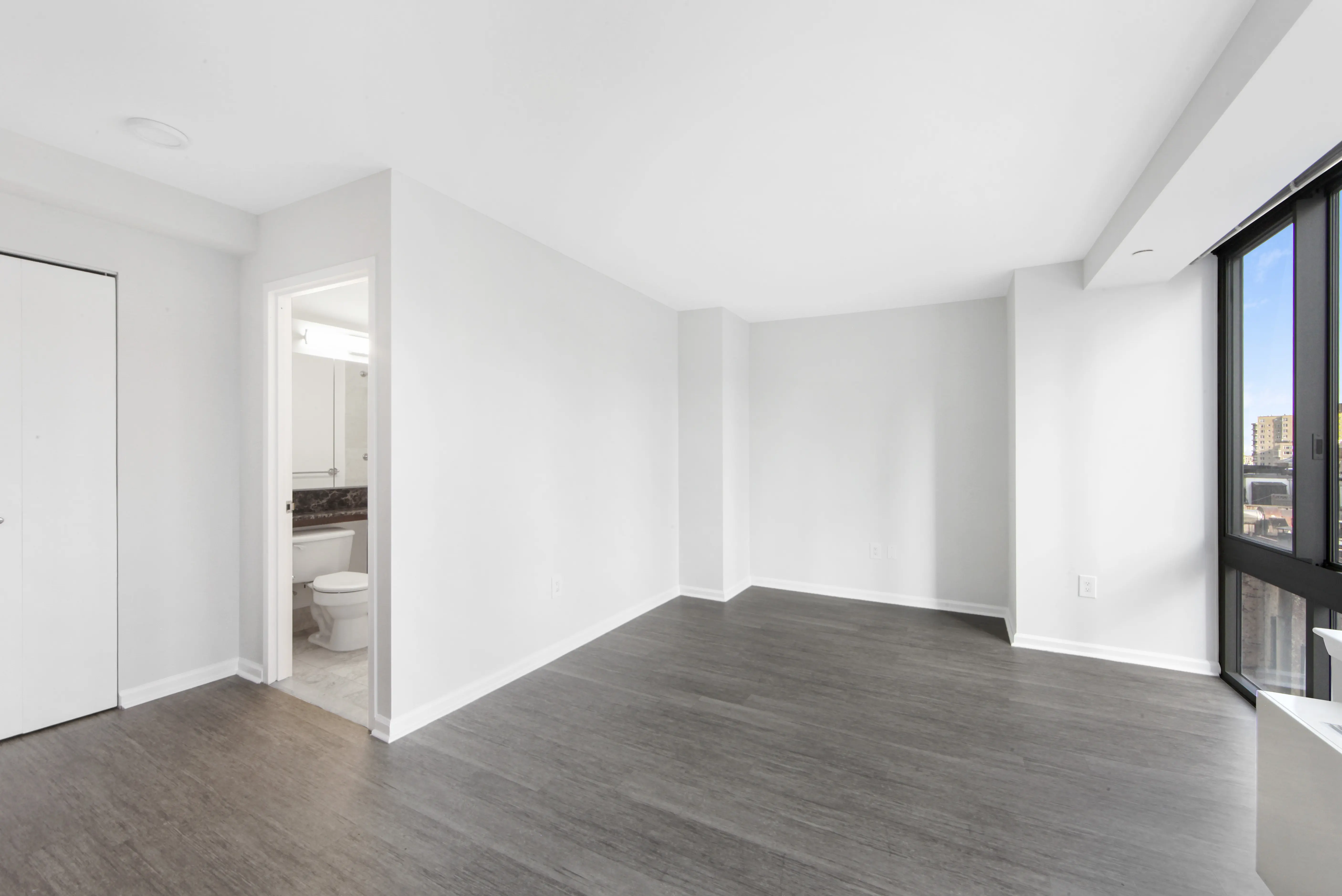 A spacious empty room featuring hardwood floors and plain white walls, creating a bright and open atmosphere.