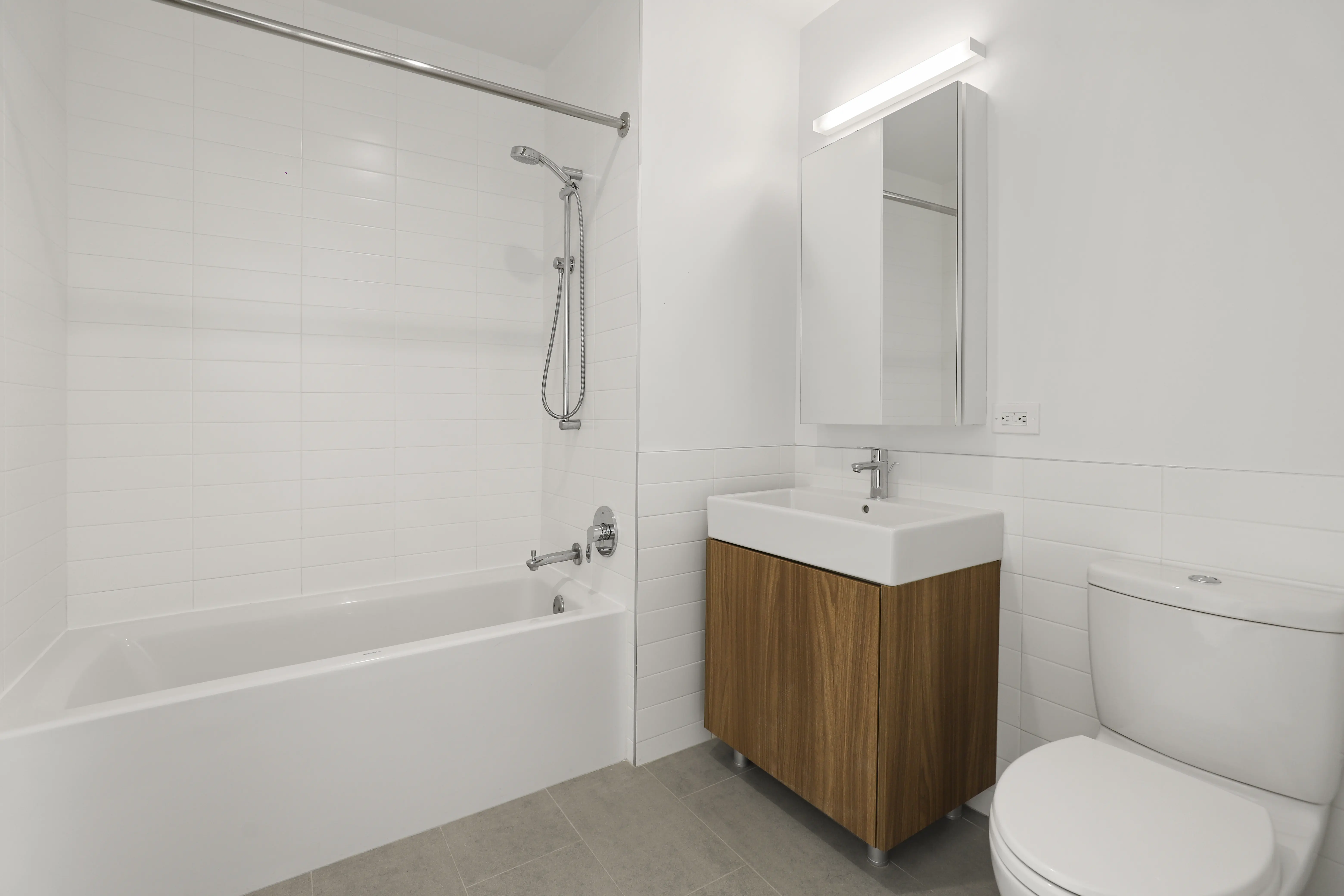 A modern bathroom with white tiled walls, including a toilet, sink, and a spacious bathtub.