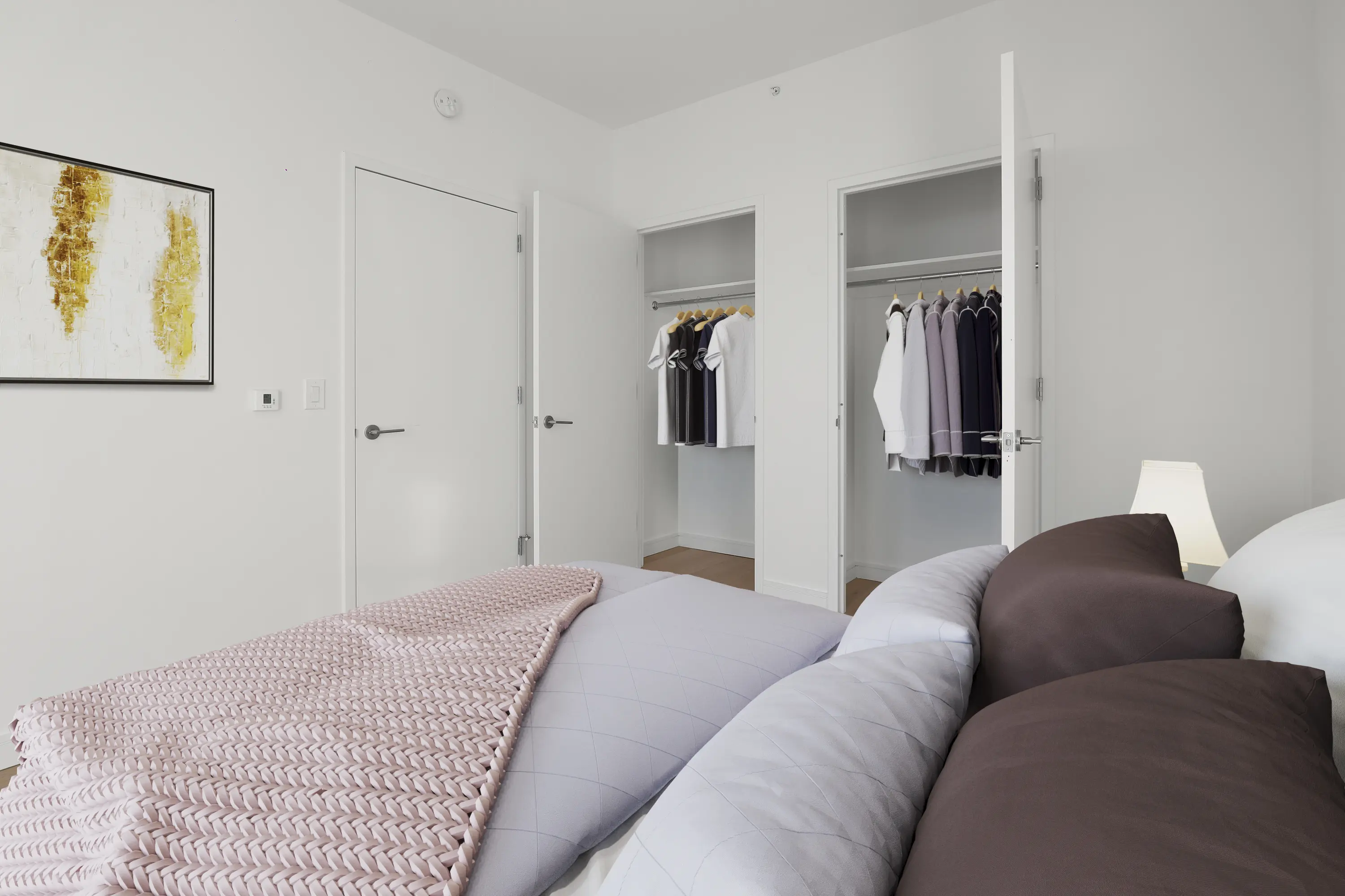 A well-furnished bedroom with a neatly made bed, a closet, and an artistic painting hanging above.