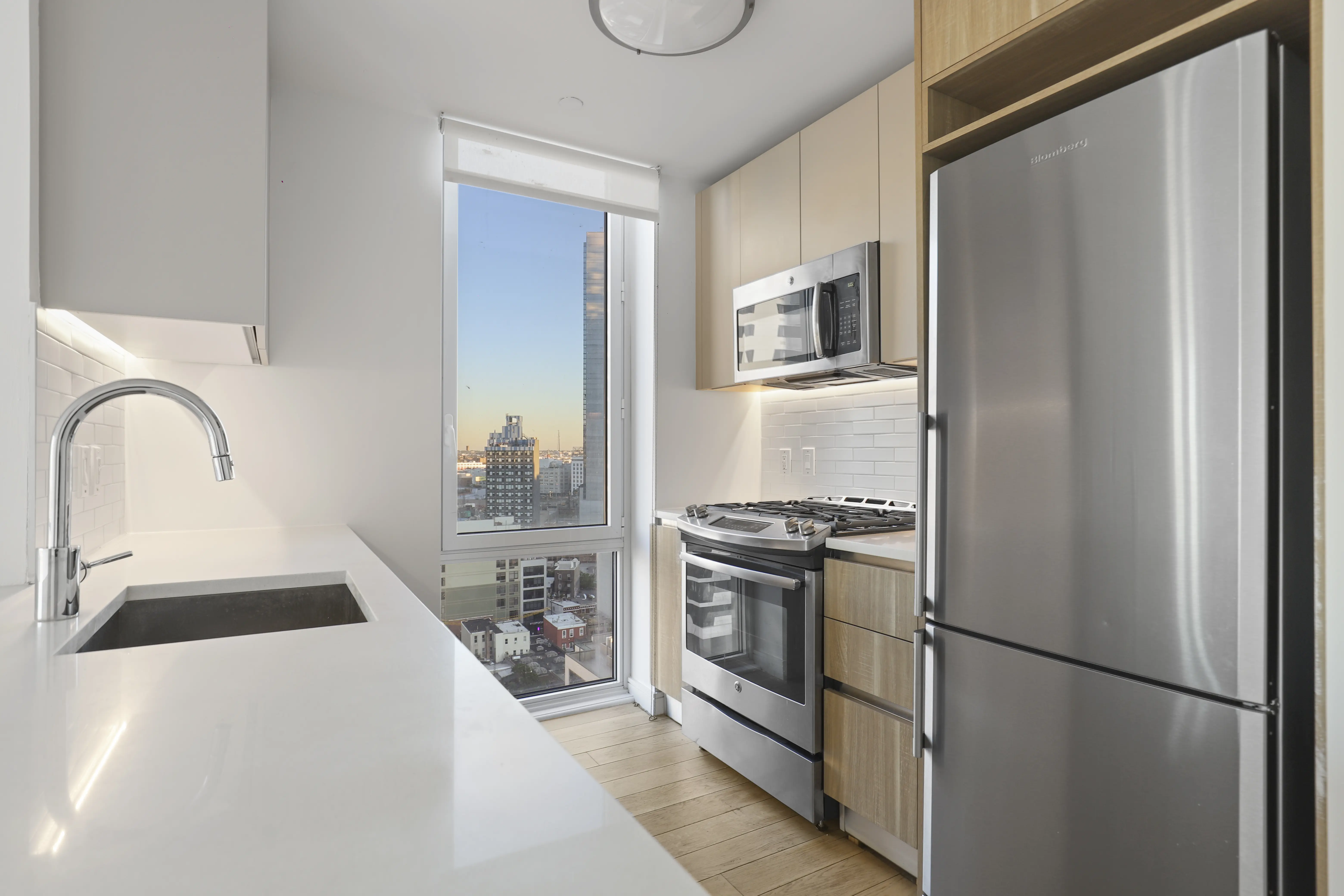 A modern kitchen featuring stainless steel appliances and a panoramic view of the city skyline through large windows.