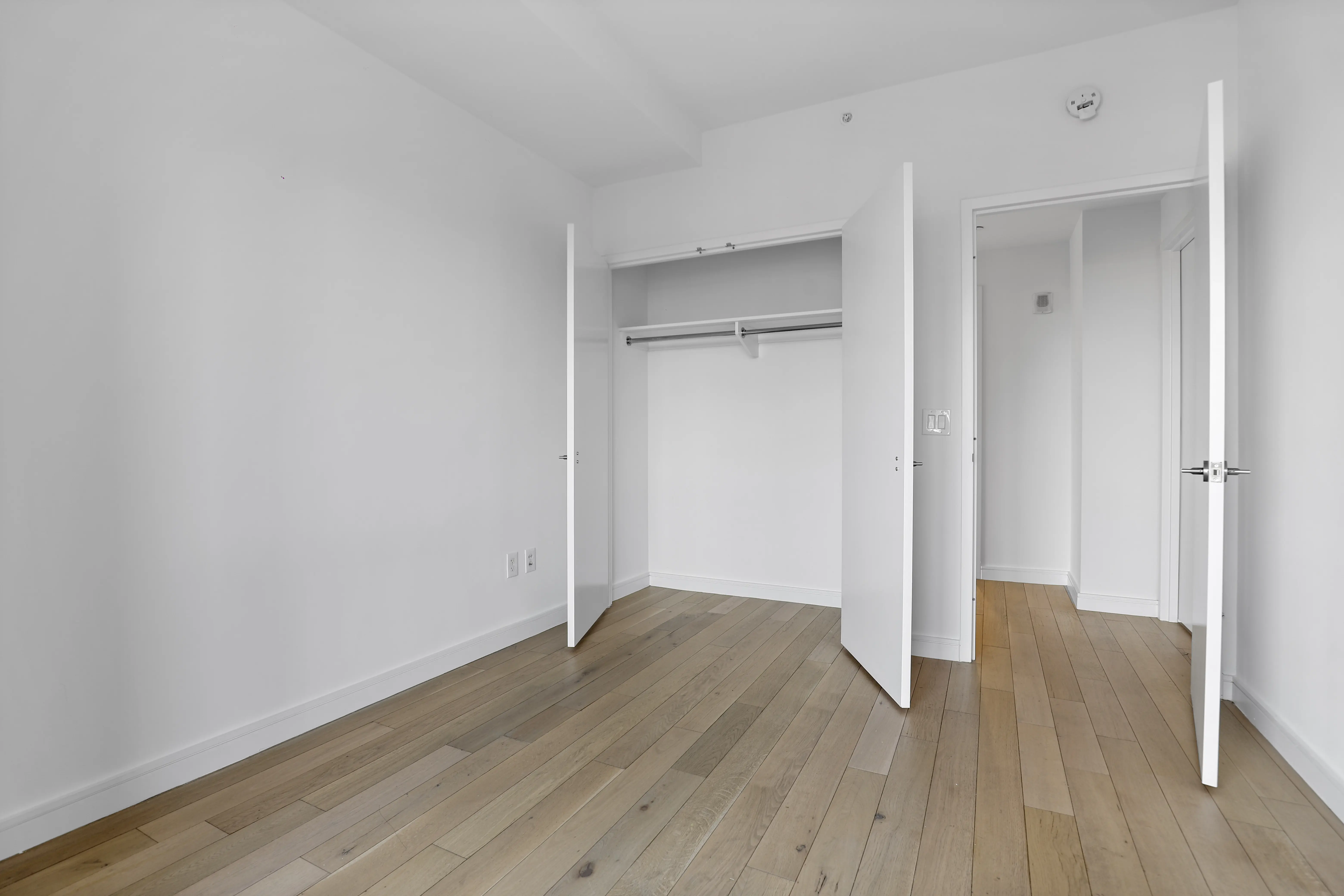 A bright white room featuring wooden floors and built-in closets along the walls.