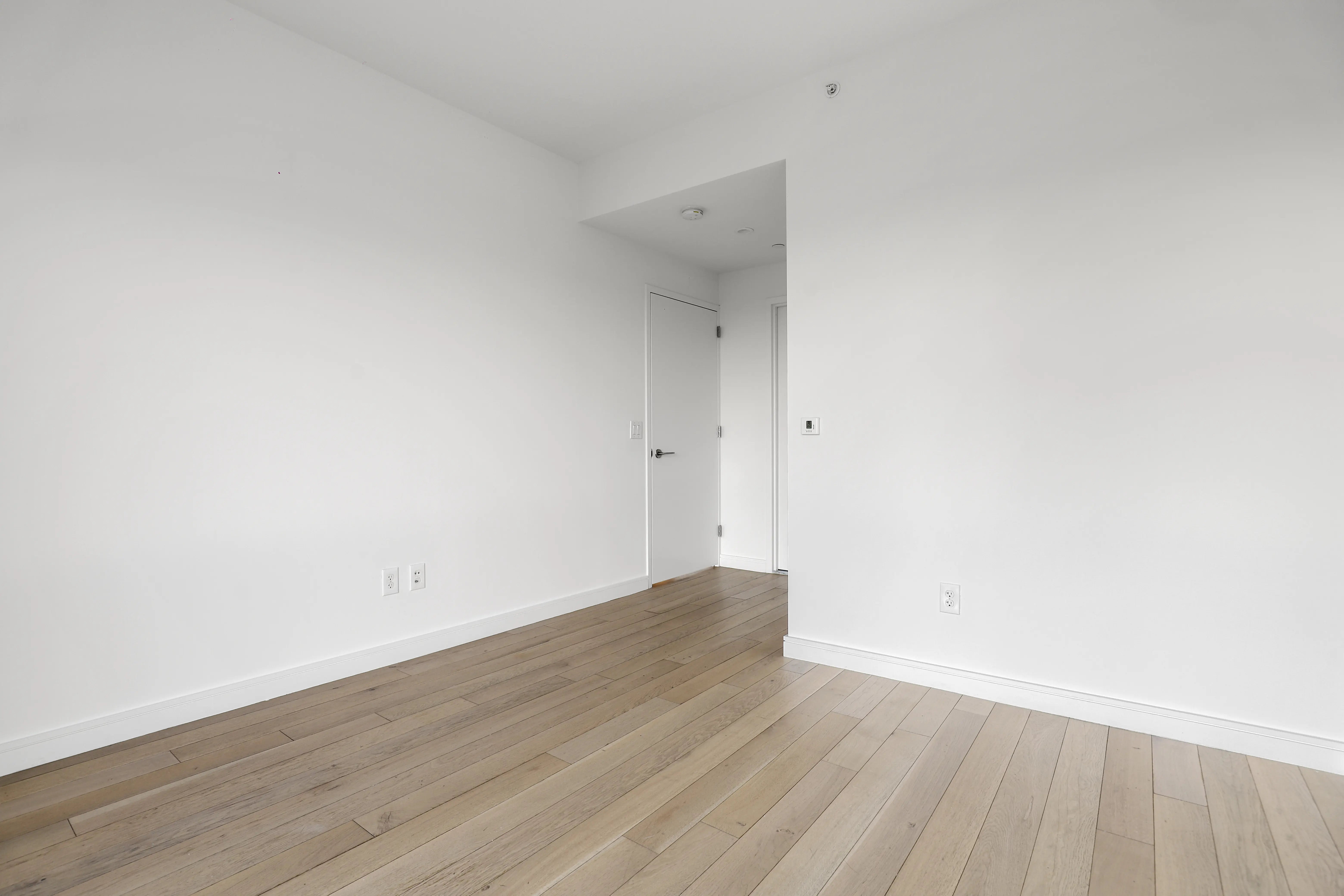 An empty room featuring white walls and polished hardwood floors, creating a bright and spacious atmosphere.