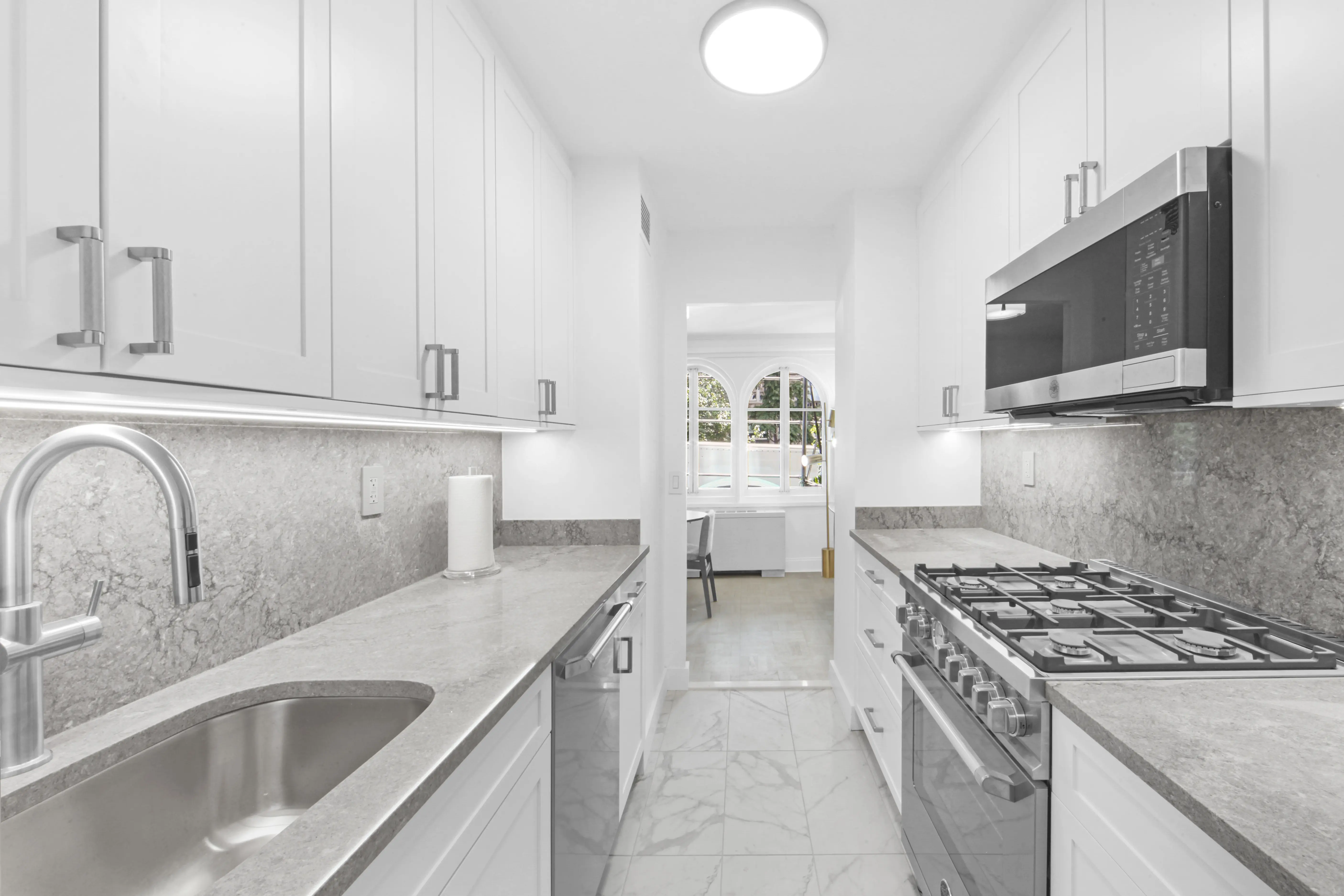 A spacious narrow kitchen adorned with white cabinets and stainless steel appliances, showcasing a clean aesthetic.