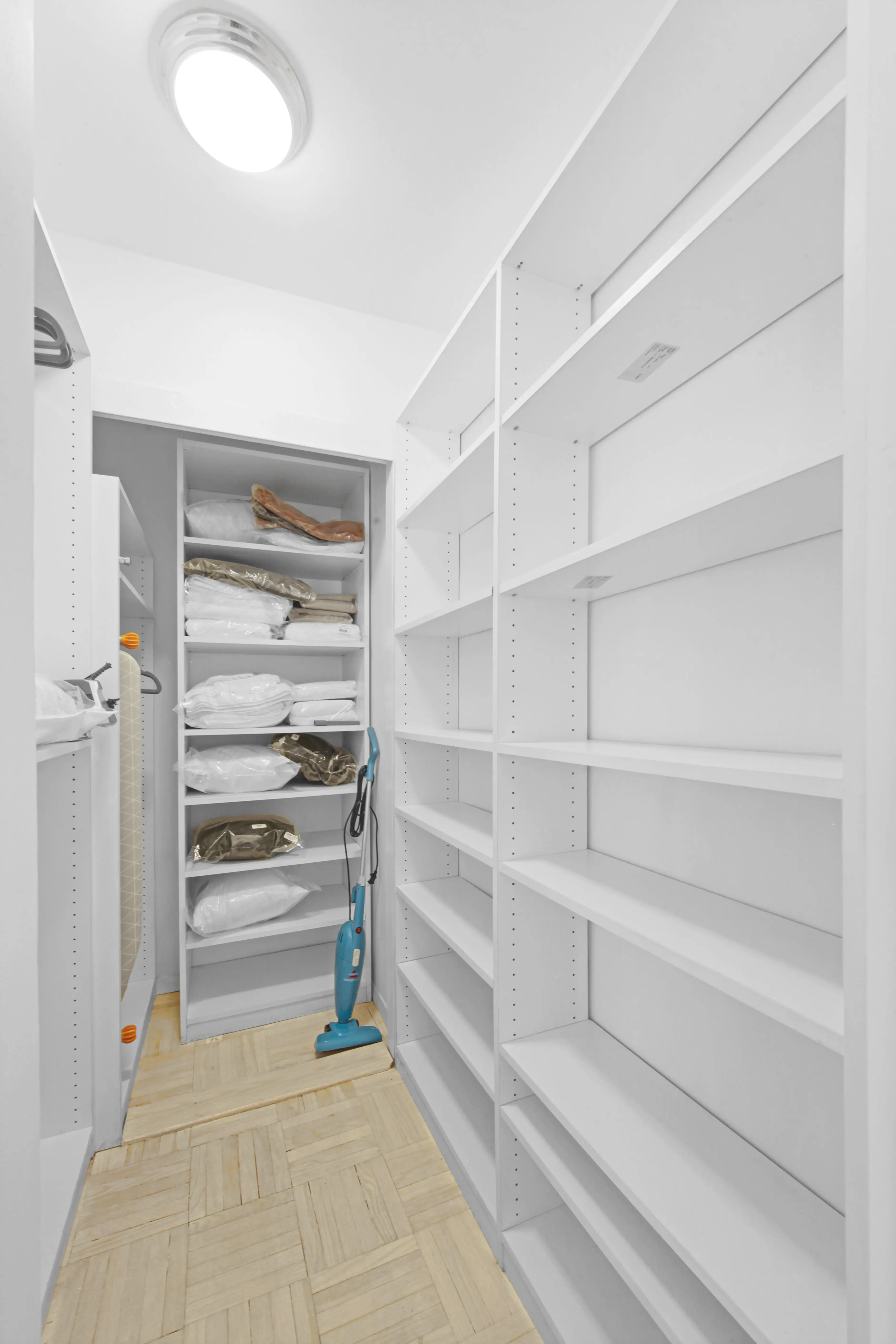 A spacious walk-in closet featuring shelves and a vacuum cleaner positioned against the wall.
