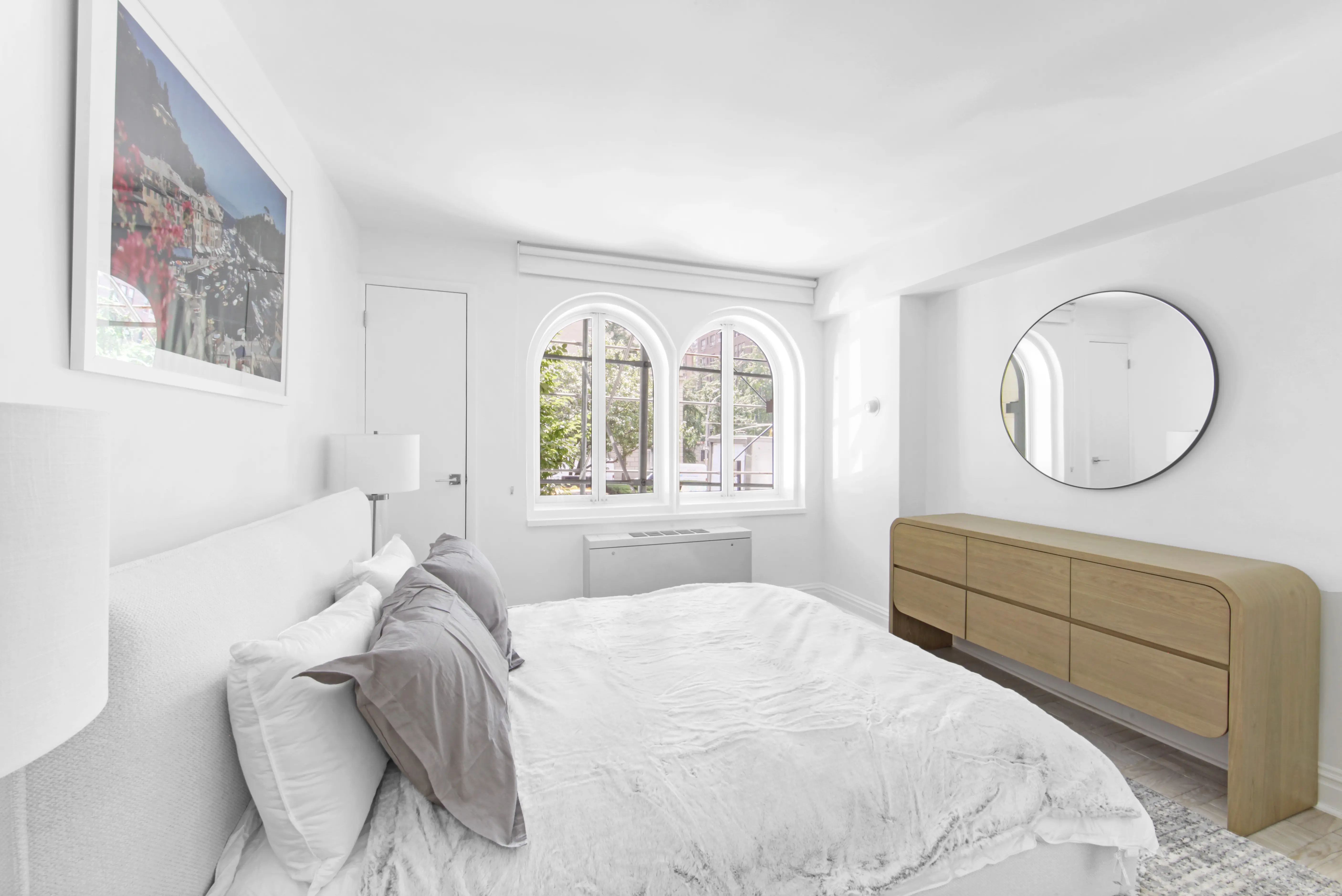 A cozy bedroom featuring a white bed and a large mirror reflecting the room's decor.