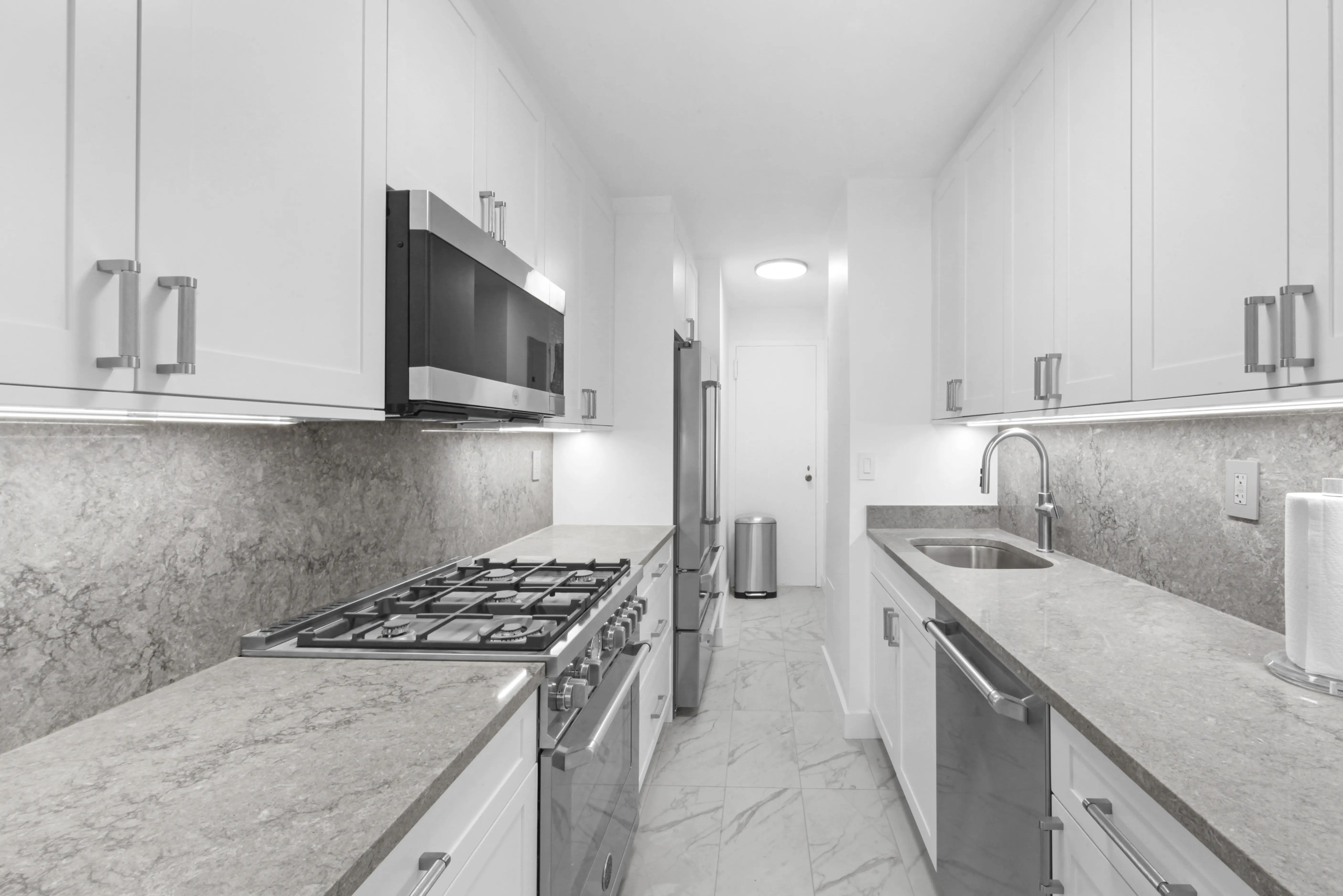 A sleek, narrow kitchen with white cabinetry and stainless steel appliances, emphasizing a contemporary design.