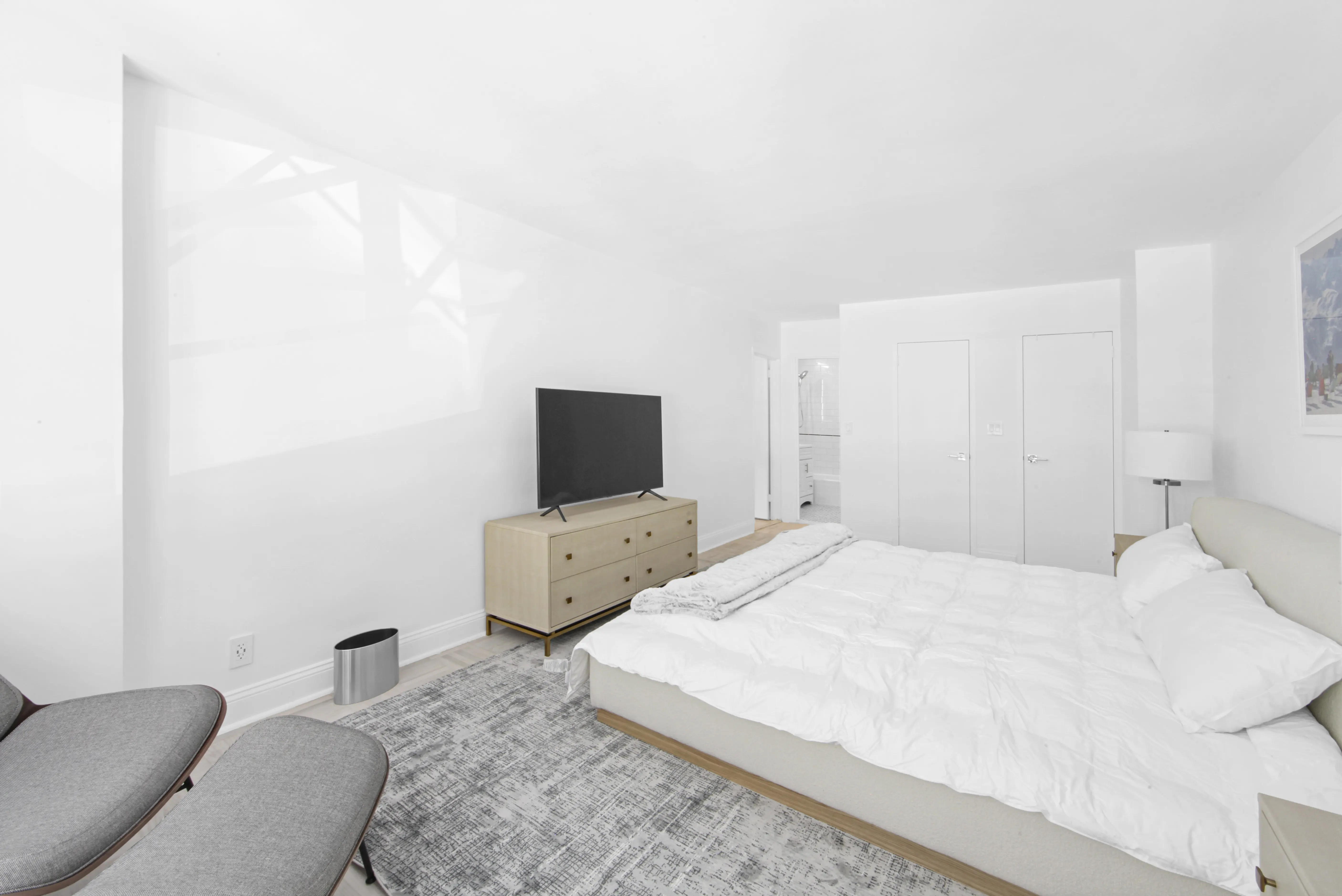 A modern bedroom showcasing a white bed and a television positioned at the foot of the bed.