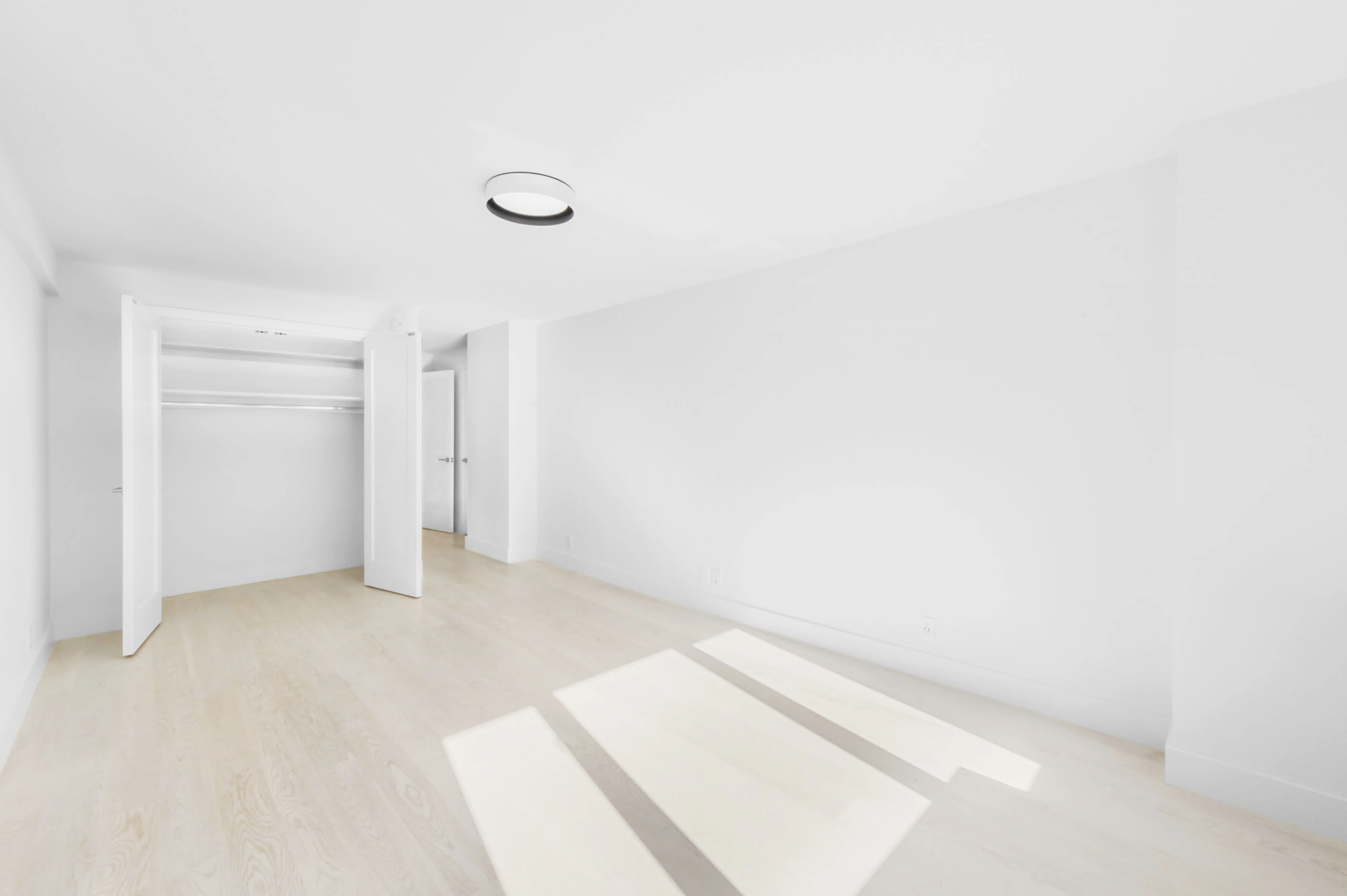 An airy white room showcasing a closet and a contemporary light fixture overhead, creating a clean aesthetic.