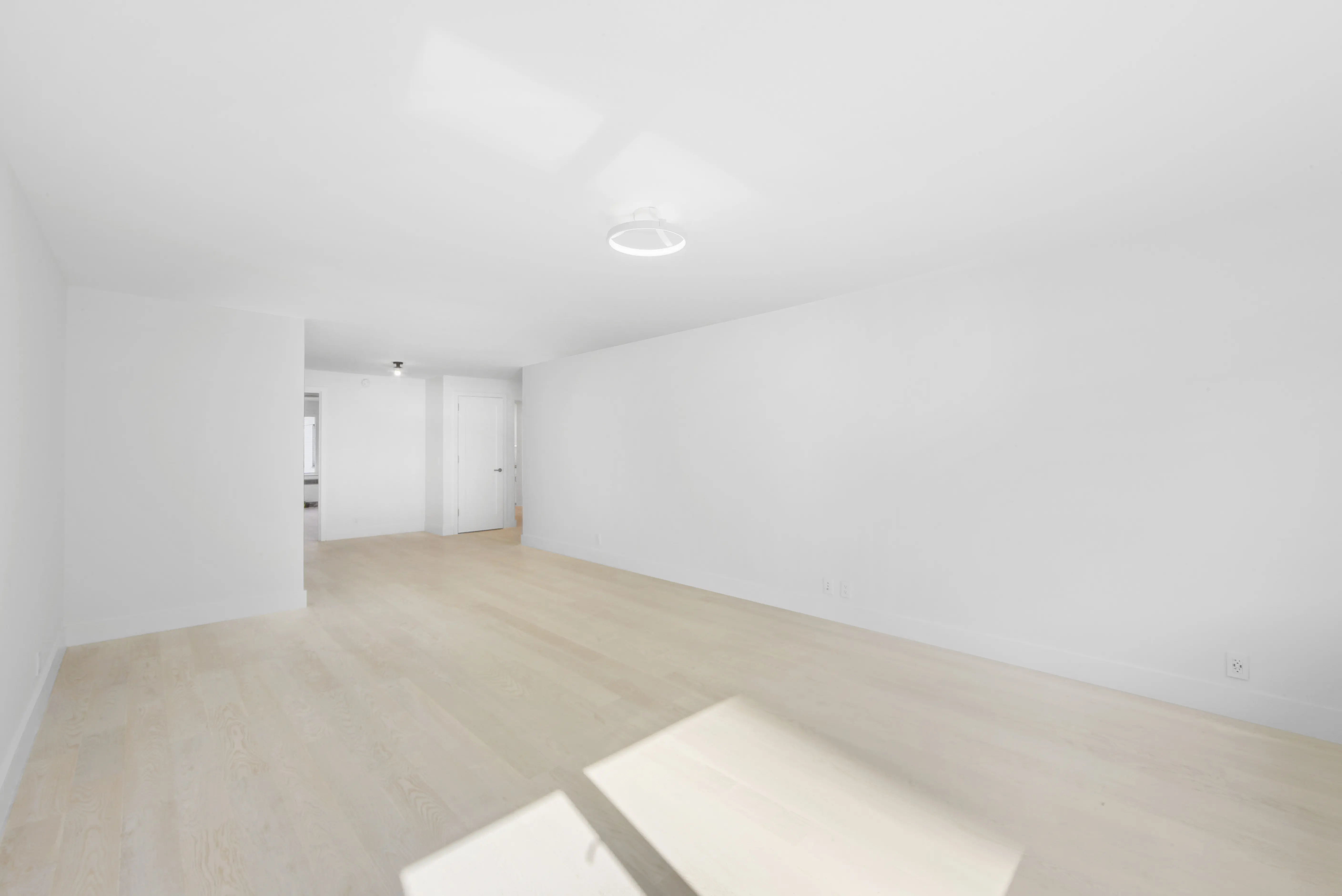 A minimalist white room with warm hardwood floors and a window, enhancing the room's brightness and openness.