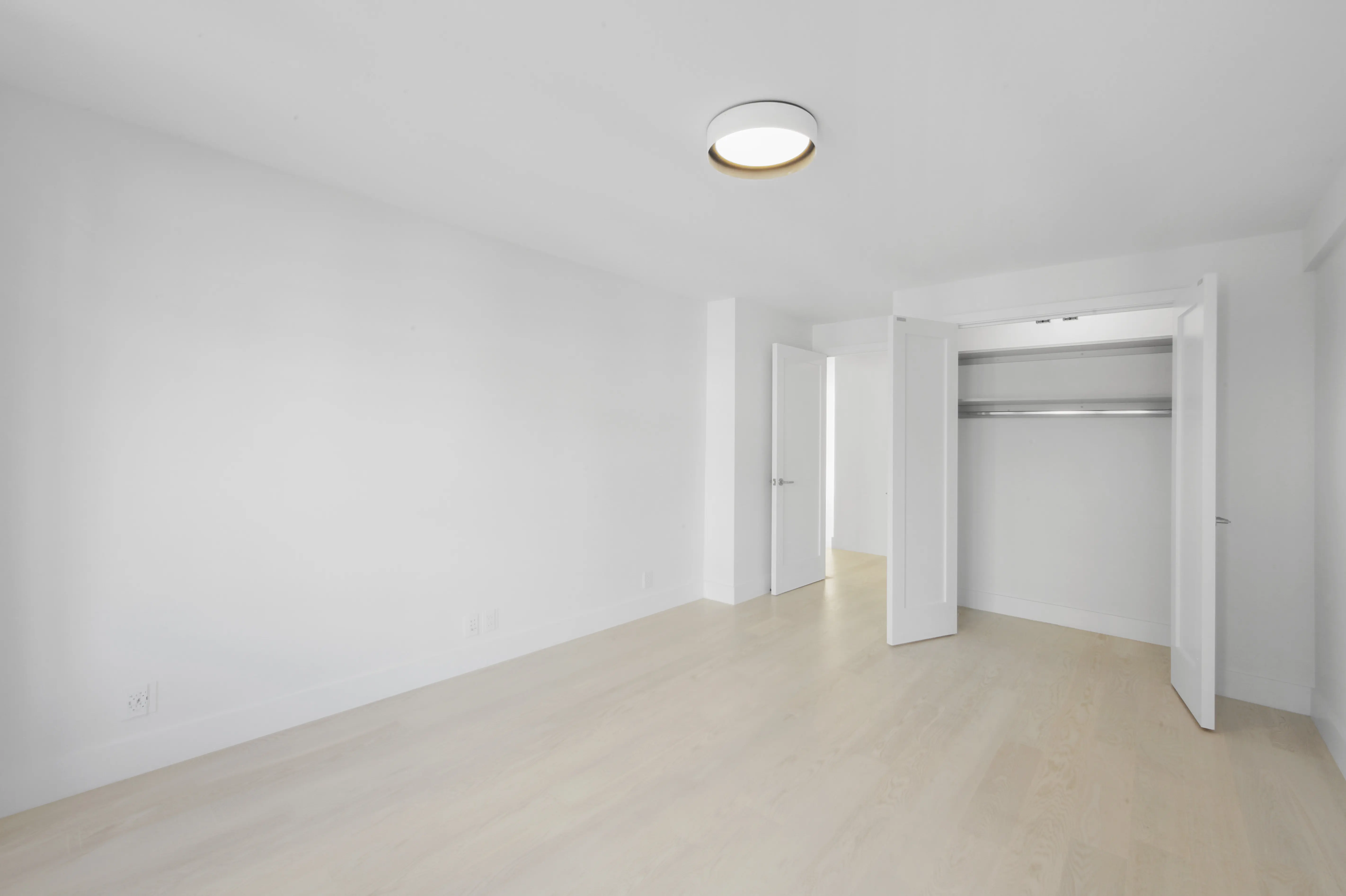 A bright white room featuring a closet and a modern light fixture hanging from the ceiling.