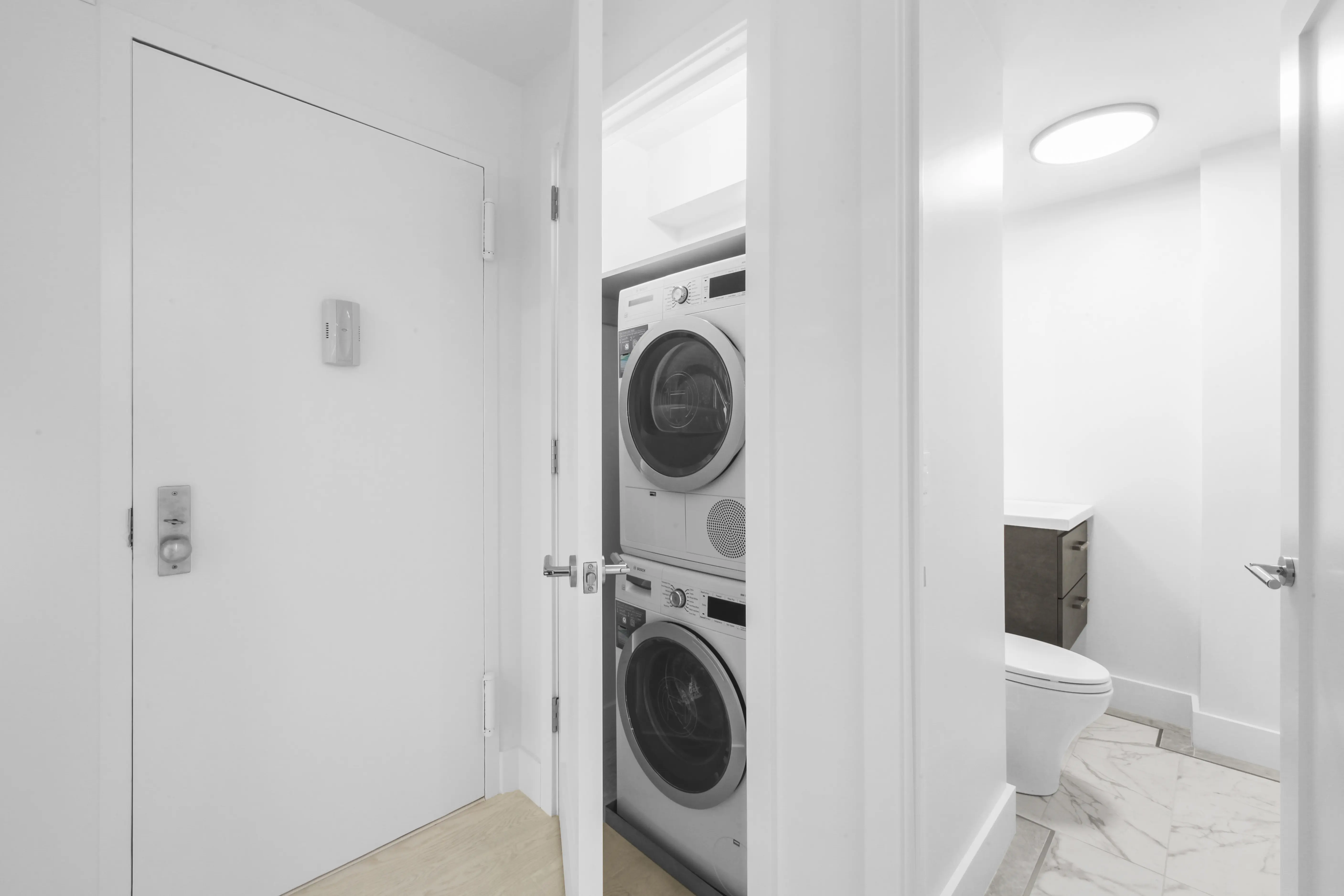 A clean white bathroom featuring a stacked washer and dryer against a bright wall.