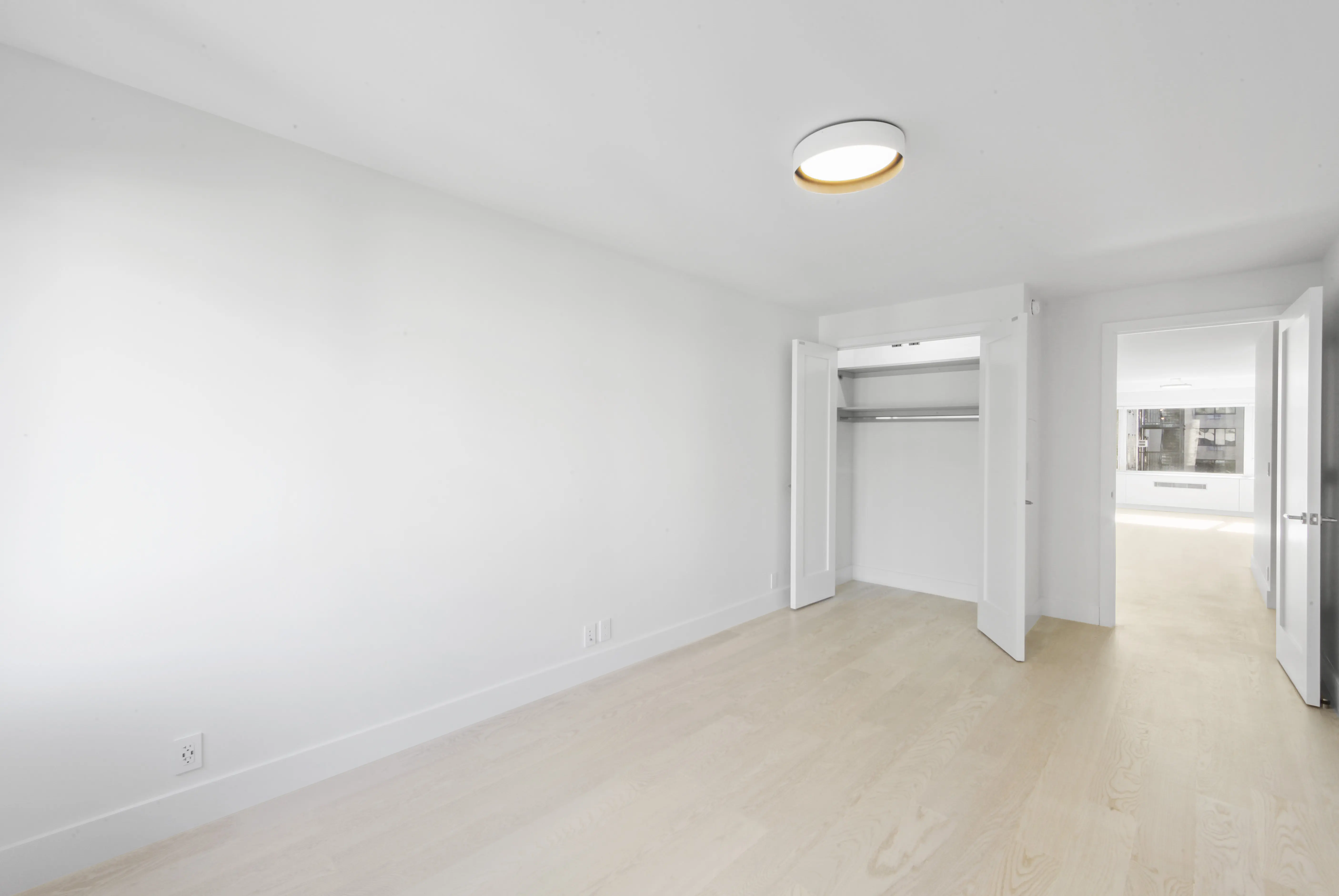 A spacious white room with a closet on one side and a stylish light fixture illuminating the space.
