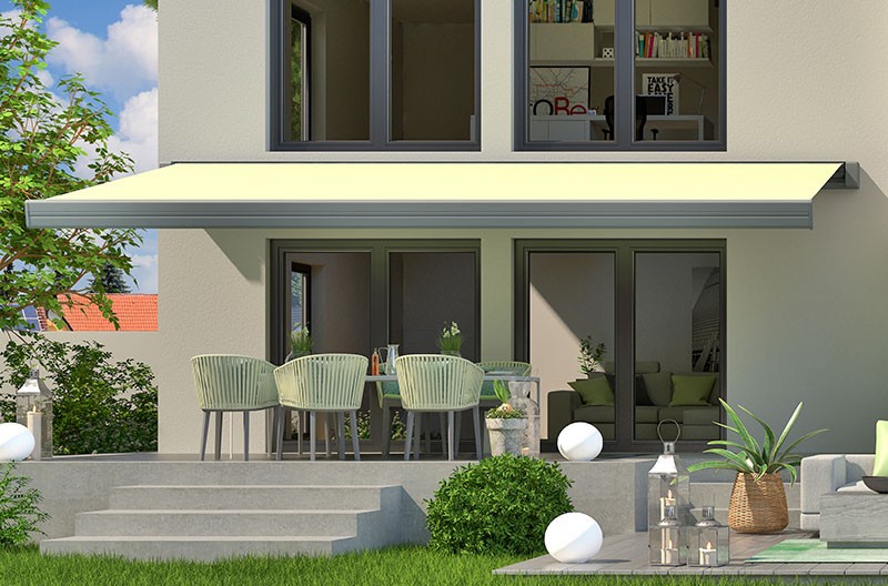 Patio with outdoor furniture and plants beside modern home with awning and sliding glass doors.