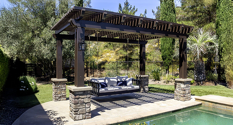Outdoor patio with pergola, seating area, and pool in a landscaped backyard with trees and grass.