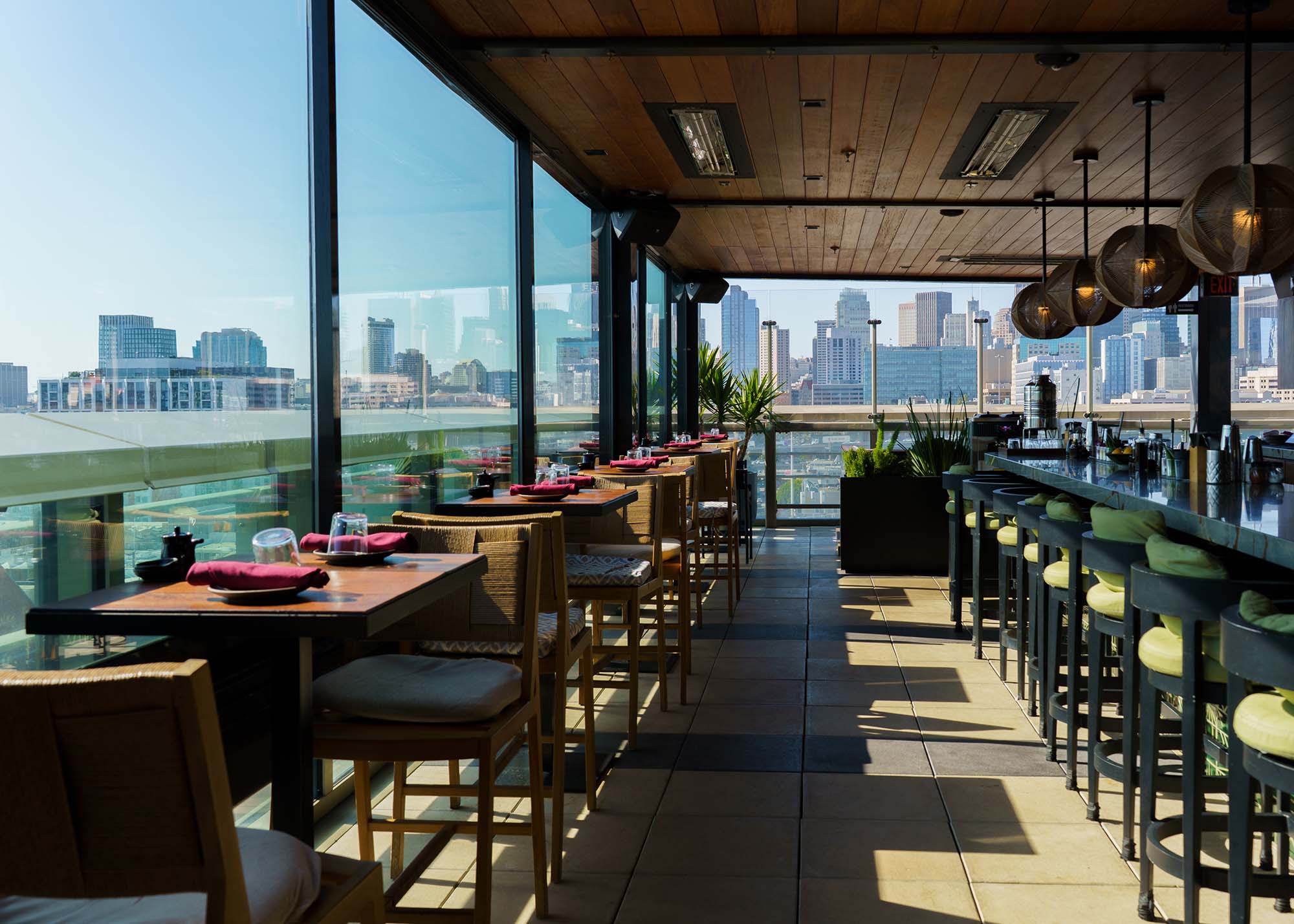 Spectacular sunset view from Kaiyō's rooftop dining area, overlooking the San Francisco skyline. The space is furnished with modern outdoor seating, tables set for dining, and decorative plants.