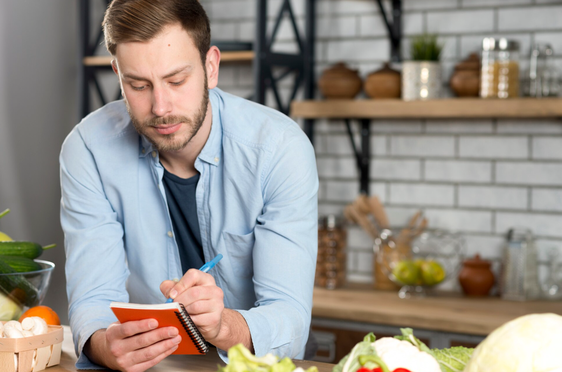 Man writing in a notebook surrounded by vegetables, symbolizing nutrition planning as part of weight loss with Ozempic treatment