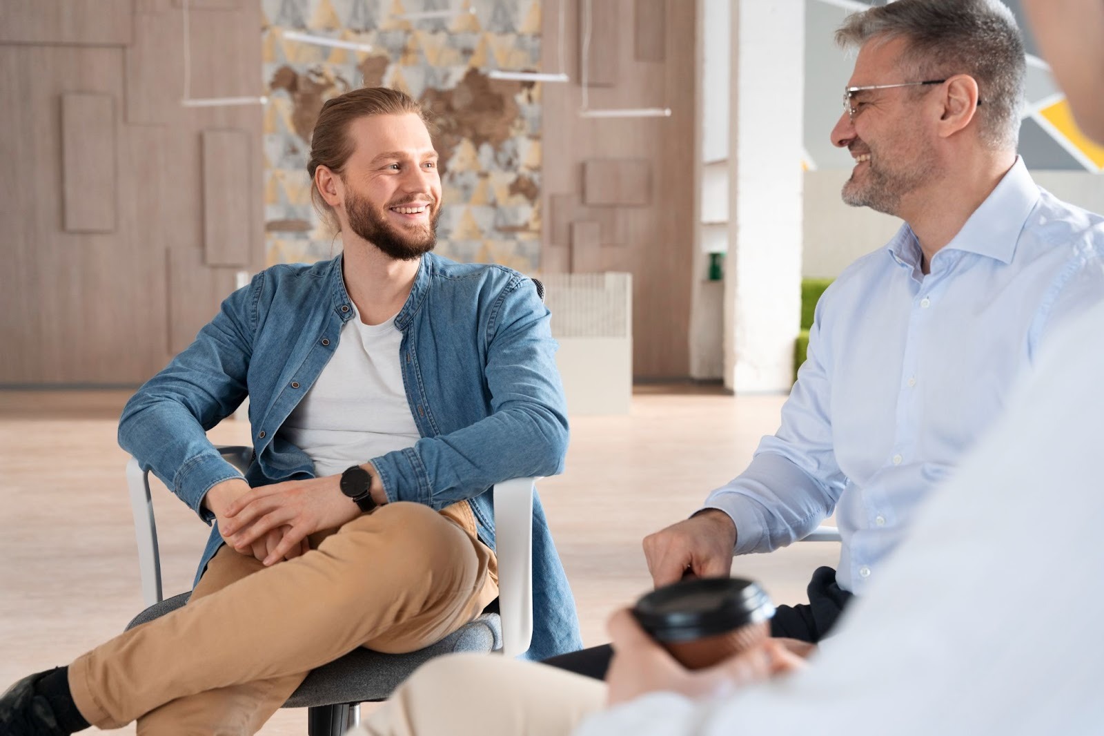 Two men of different ages sitting and smiling while talking in a bright office setting, representing open conversations about men’s health and testosterone levels
