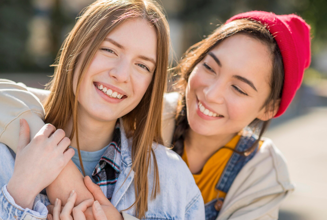 Two young women happily hugging each other, both smiling warmly