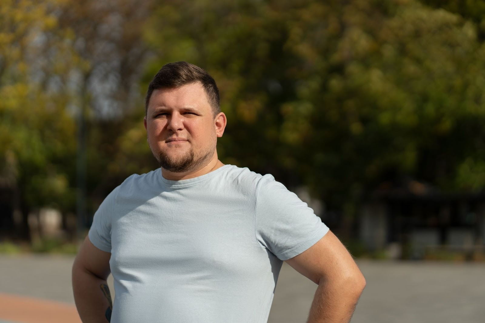 A slightly obese man looking directly at the camera against a forest or a park backdrop