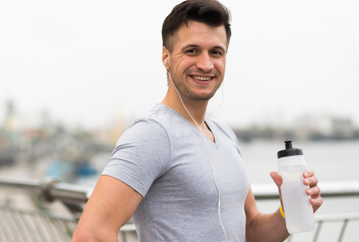 A healthy and fit ma drinking water and wearing earphones looking at the camera