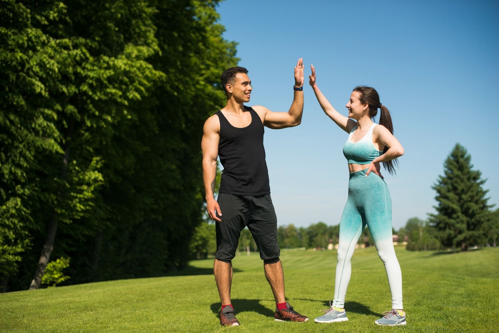 A fit and healthy looking man and woman doing a high five in a park